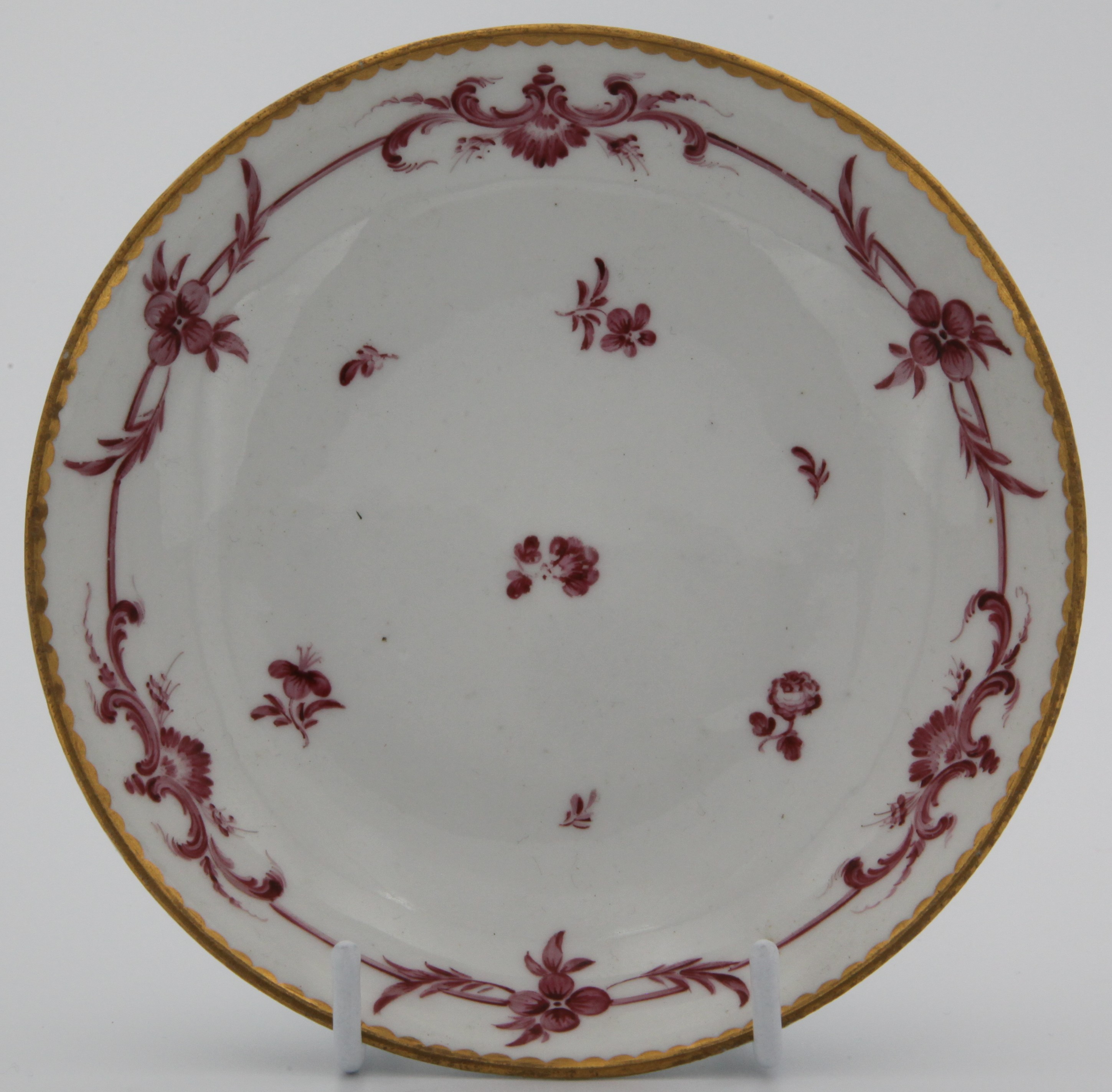 A fine Bristol saucer painted with monochrome puce scroll band with scattered flowers under gilt dentil rim. Mark: dark blue crossed swords and gilt 6.
