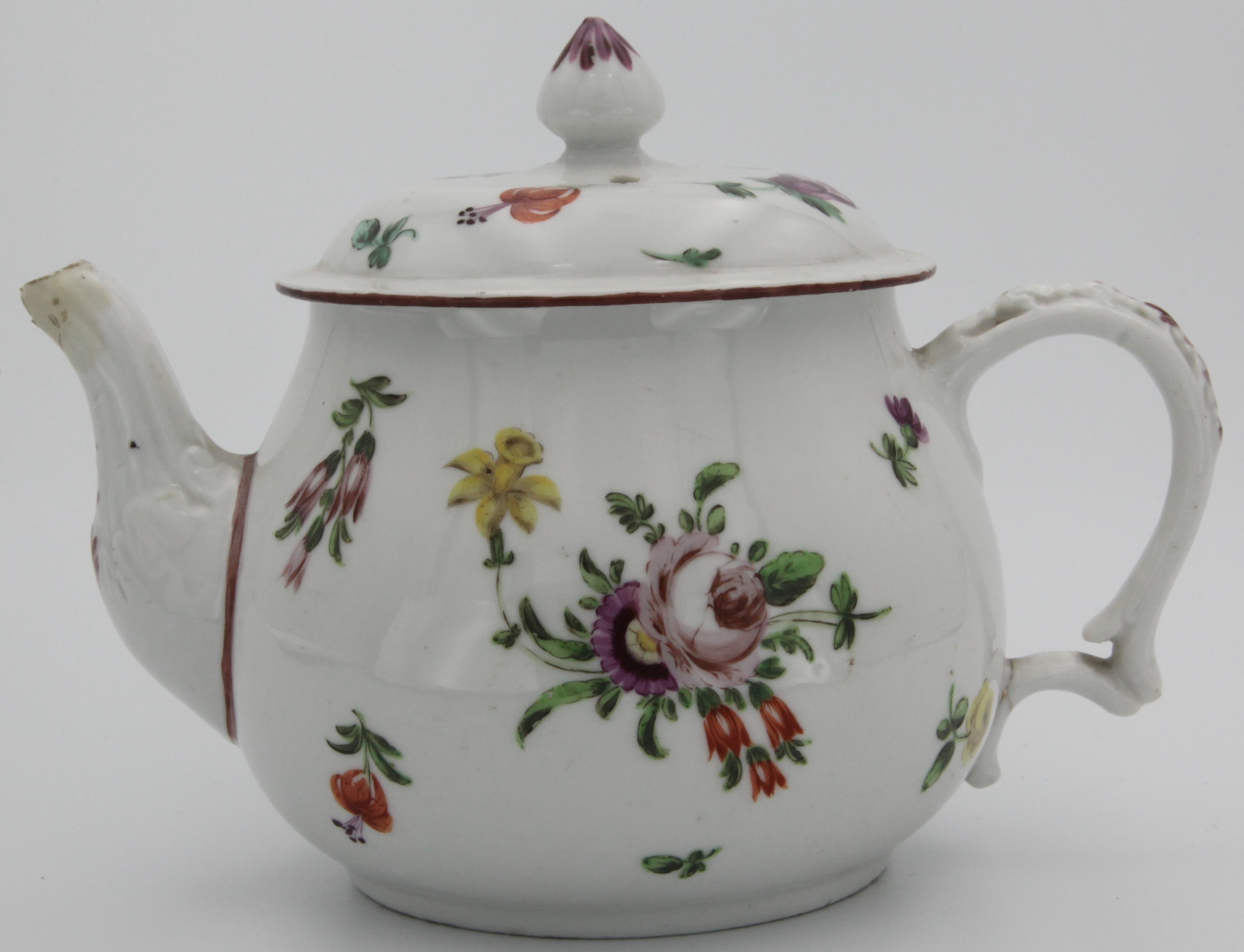 A small Bristol teapot and cover, with moulded handle, conical purple-painted finial to cover, painted with colourful sprays and scattered leaves and flowers, iron red rim. No mark