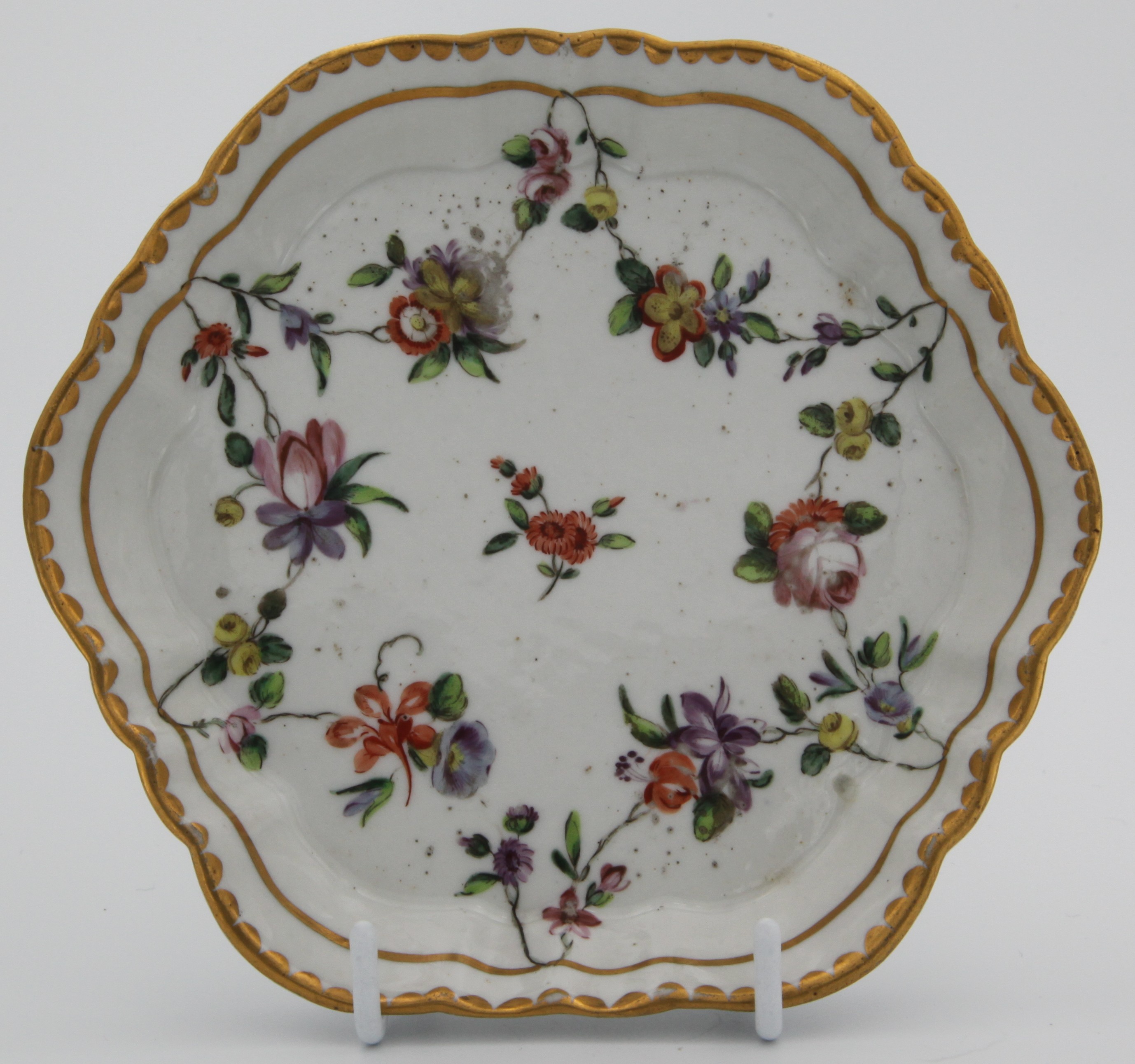 An fluted Bristol hexagonal sucrier stand, painted in enamels with garlands of colourful flowers and leaves suspended from a gilt line, gilt dentil border, blue  X10. mark, c.1770