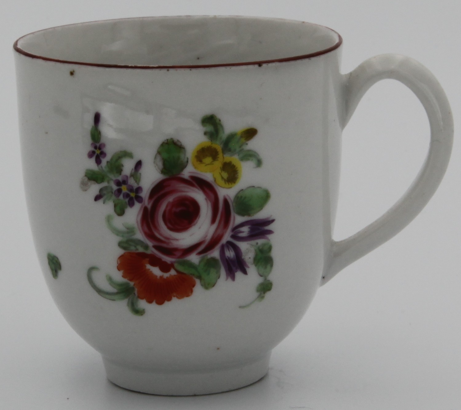 A Bristol coffee cup with plain handle, painted with a spray of purple, pink and two orange flowers, the reverse with scattered flowers and leaves, and an iron red line rim. No mark but painting matches 7. painted in blue to base. Circa 1772