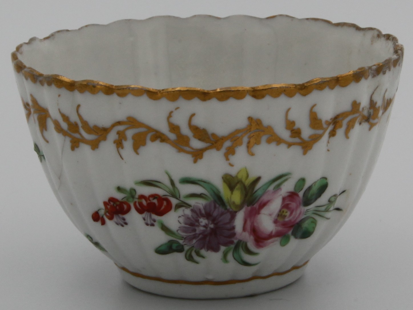 A Bristol fluted tea bowl, painted in colourful enamels with floral sprays and scattered sprigs, an elaborate leafy gilt scrolled border below the gilt dentil rim, blue X mark.