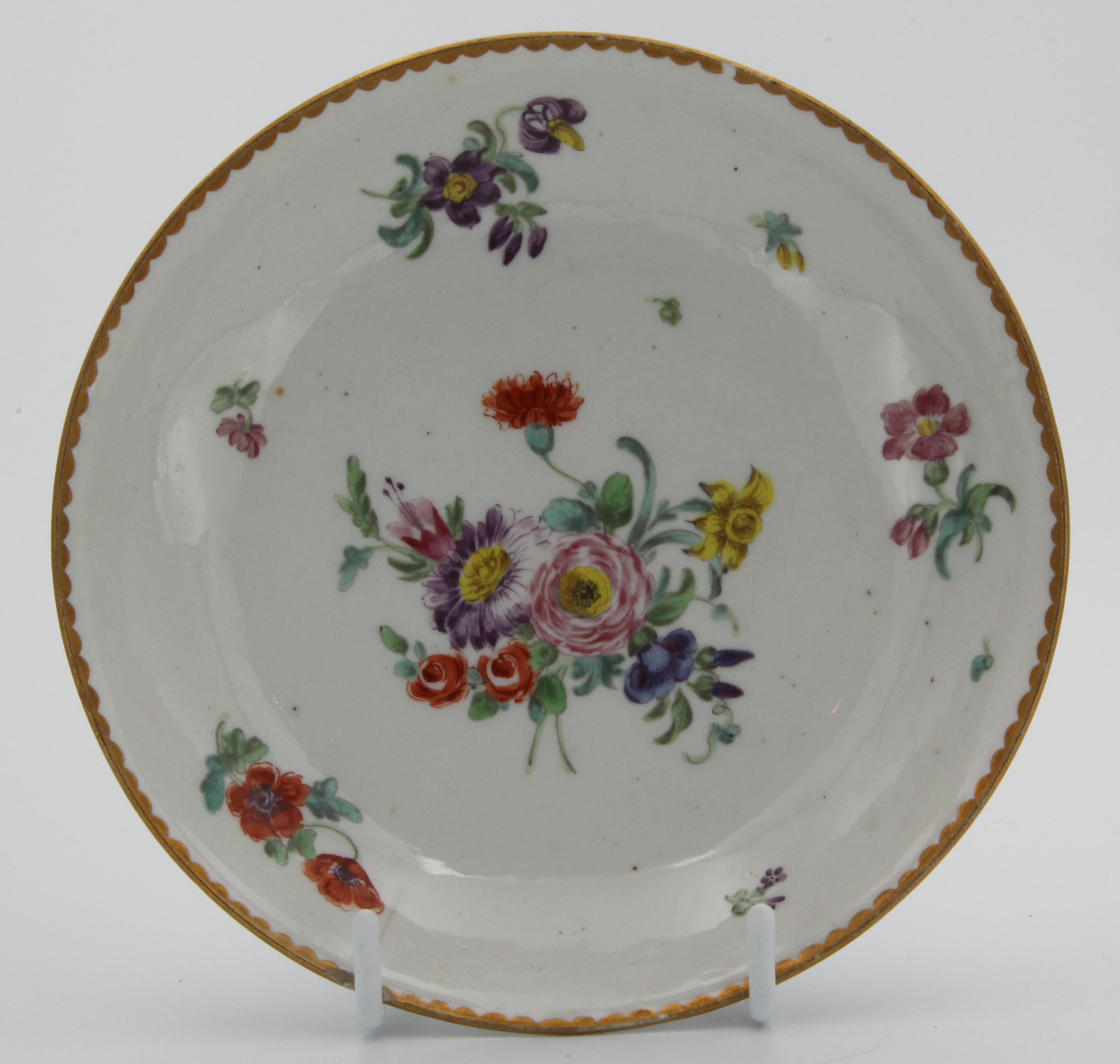 A Bristol saucer, painted in enamels with a colourful floral spray and scattered sprigs, gilt dentil rim, underglaze crossed swords mark