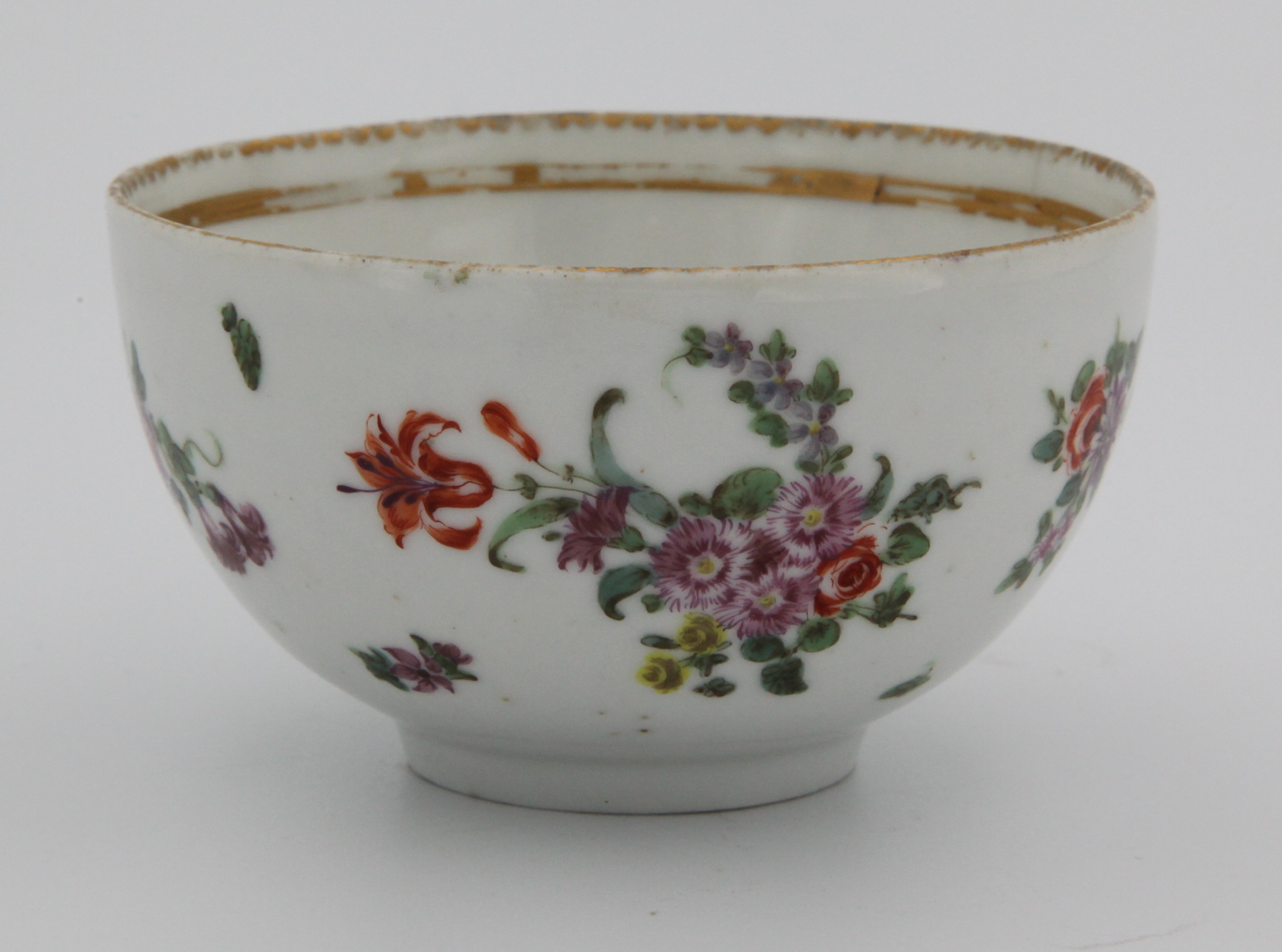 A Bristol tea cup, with moulded twig handle, painted in colourful enamels with a central spray with prominent oraneg flower and scattered sprays and leaves inside a thick gilt band, surrounded by gilt dentil rim, c.1770. No mark
