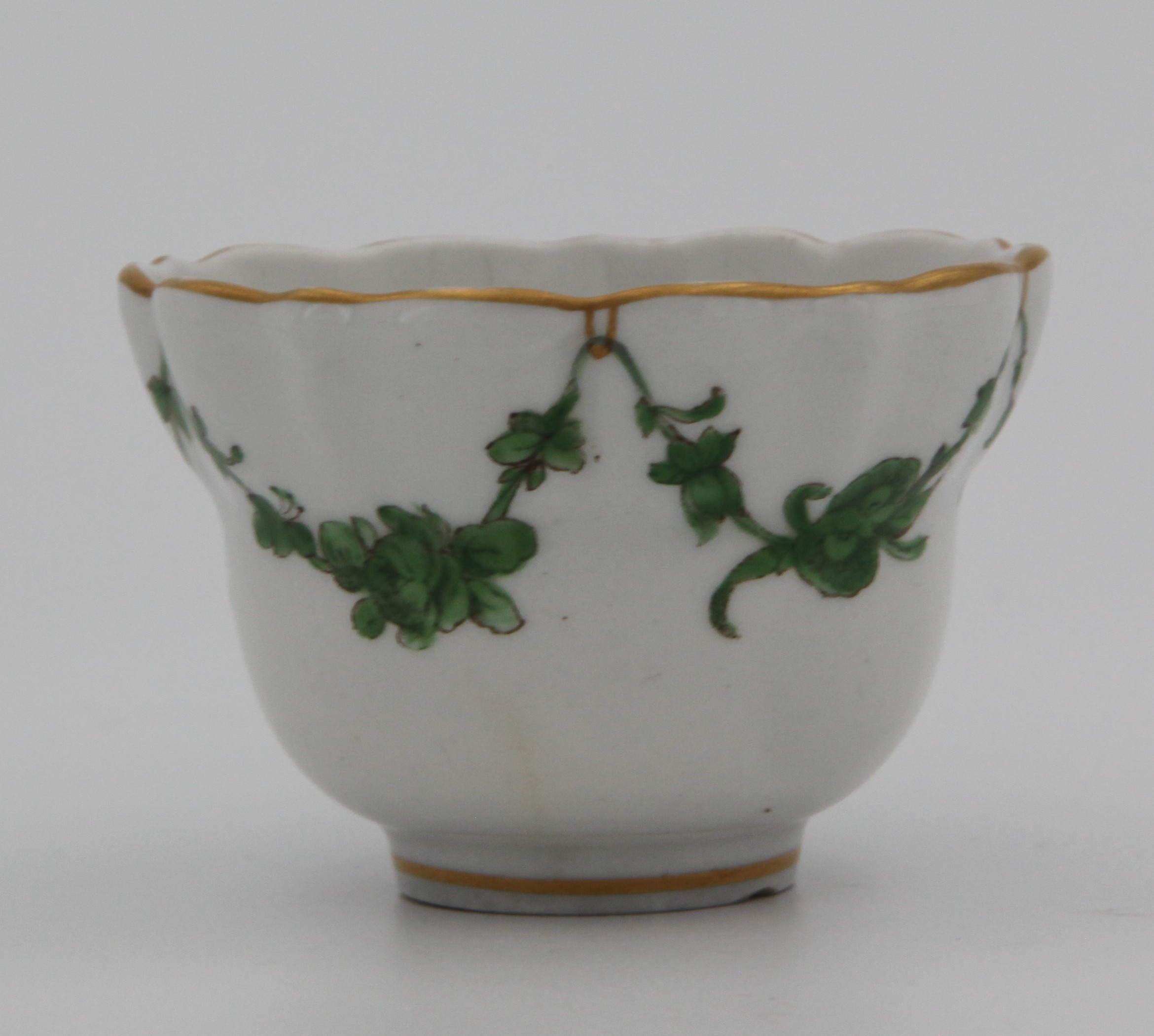 A Bristol lobed, ogee-shaped teabowl painted with green monochrome garlands of flowers and leaves suspended from gilt loops on gilt rim. Mark X10