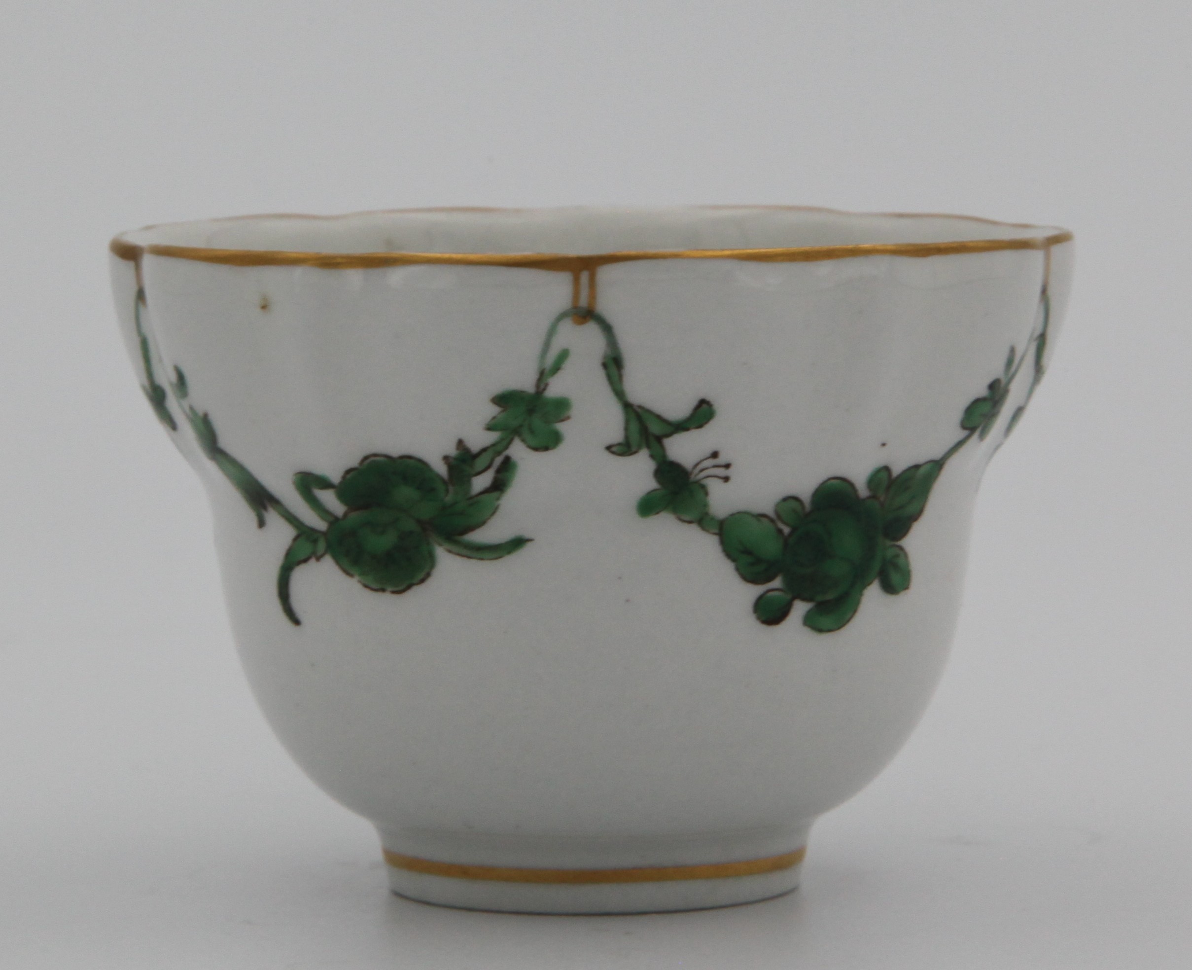 A Bristol lobed, ogee-shaped teabowl painted with green monochrome garlands of flowers and leaves suspended from gilt loops on gilt rim. Mark X10