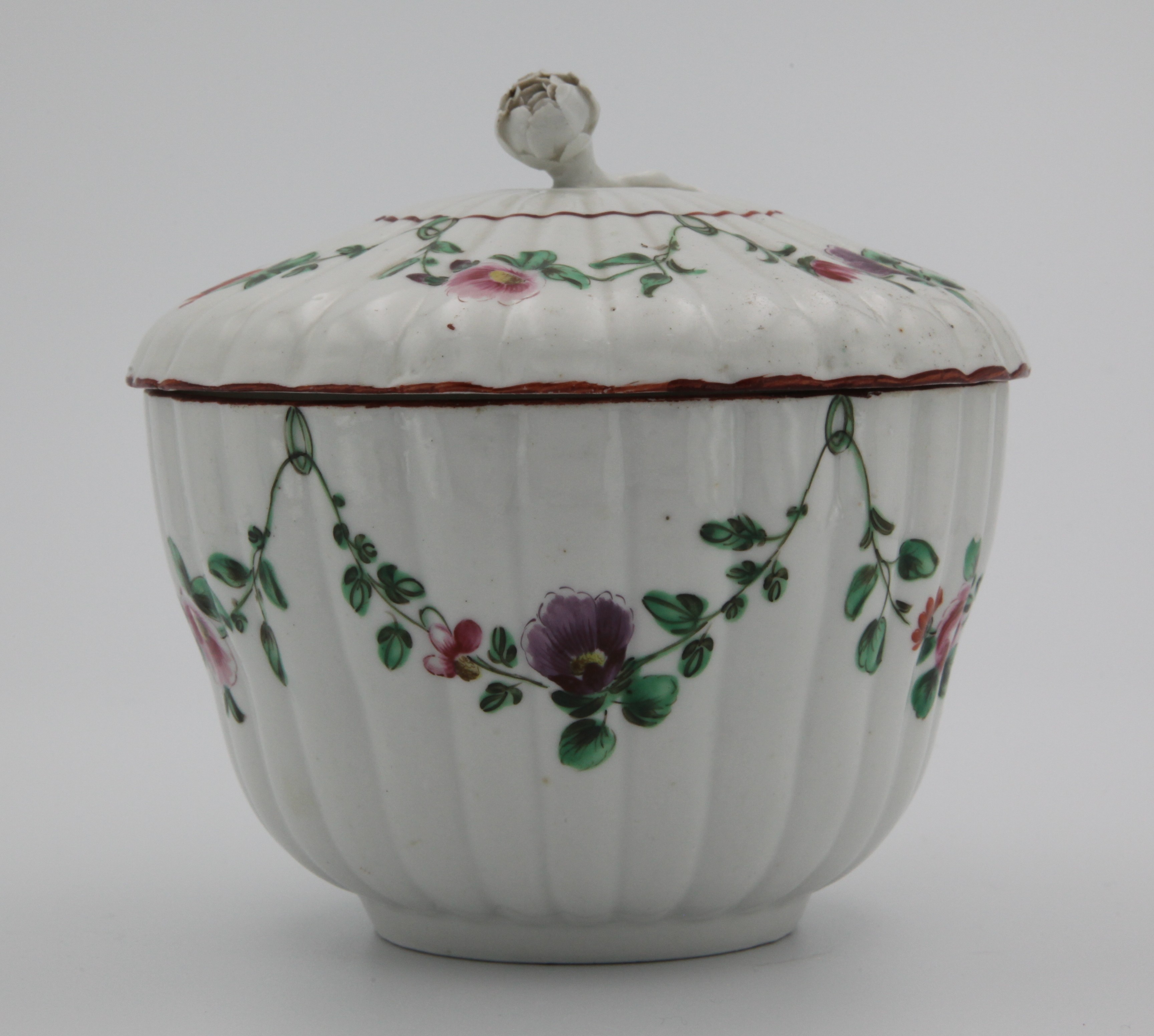 A fluted Bristol porcelain sucrier and cover with finely moulded bud finial, painted in enamels with garlands of flowers and leaves suspended from green loops hanging from a red rim line. Mark X17