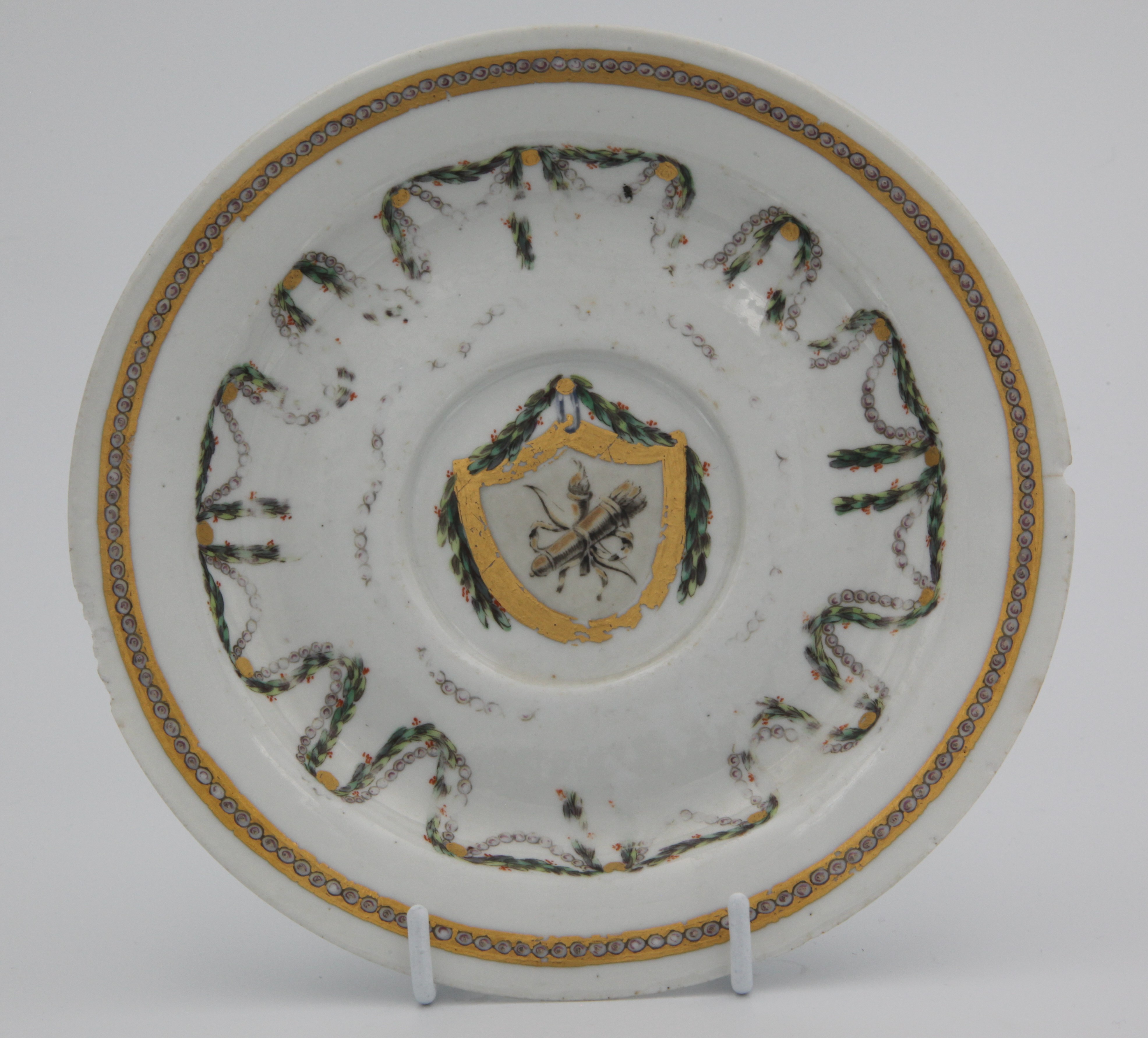 A rather sad old Bristol saucer with much gilt and decoration worn, but formerly featuring the symbol of Love in a gilt shield with laurel festoons and chains suspended from gilt roundels, all surrounded be an embellished gilt band. Mark blue X1. gilt. A perhaps redeeming feature is that it was in similar condition when it was photographed for the Trapnell catalogue (no. 349) in 1912