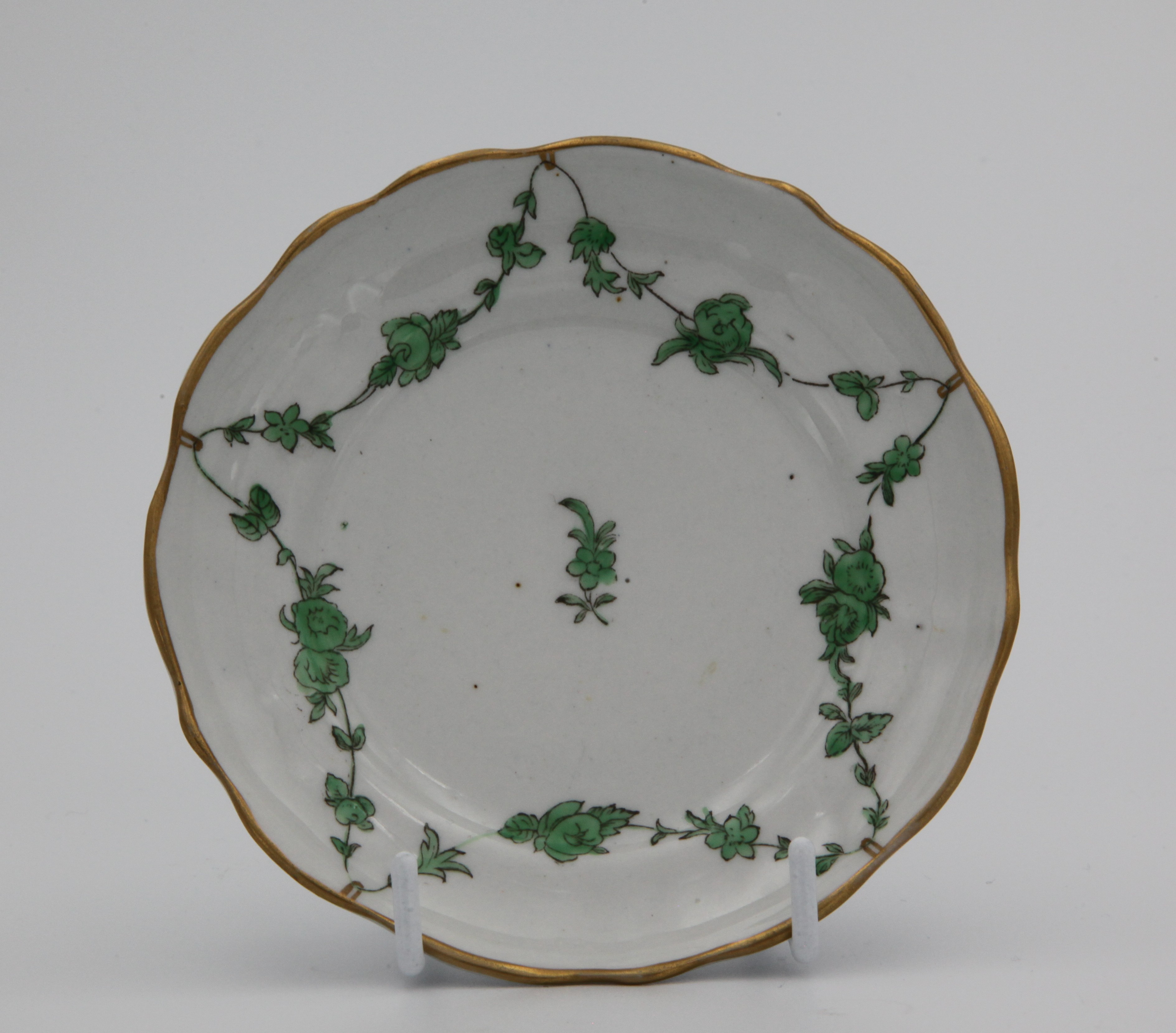 A Bristol saucer of ogee shape and with lobed rim, painted in enamels with light green garlands of leaves and flowers suspended from gilt loops hanging from a gilt rim line, Mark blue X10