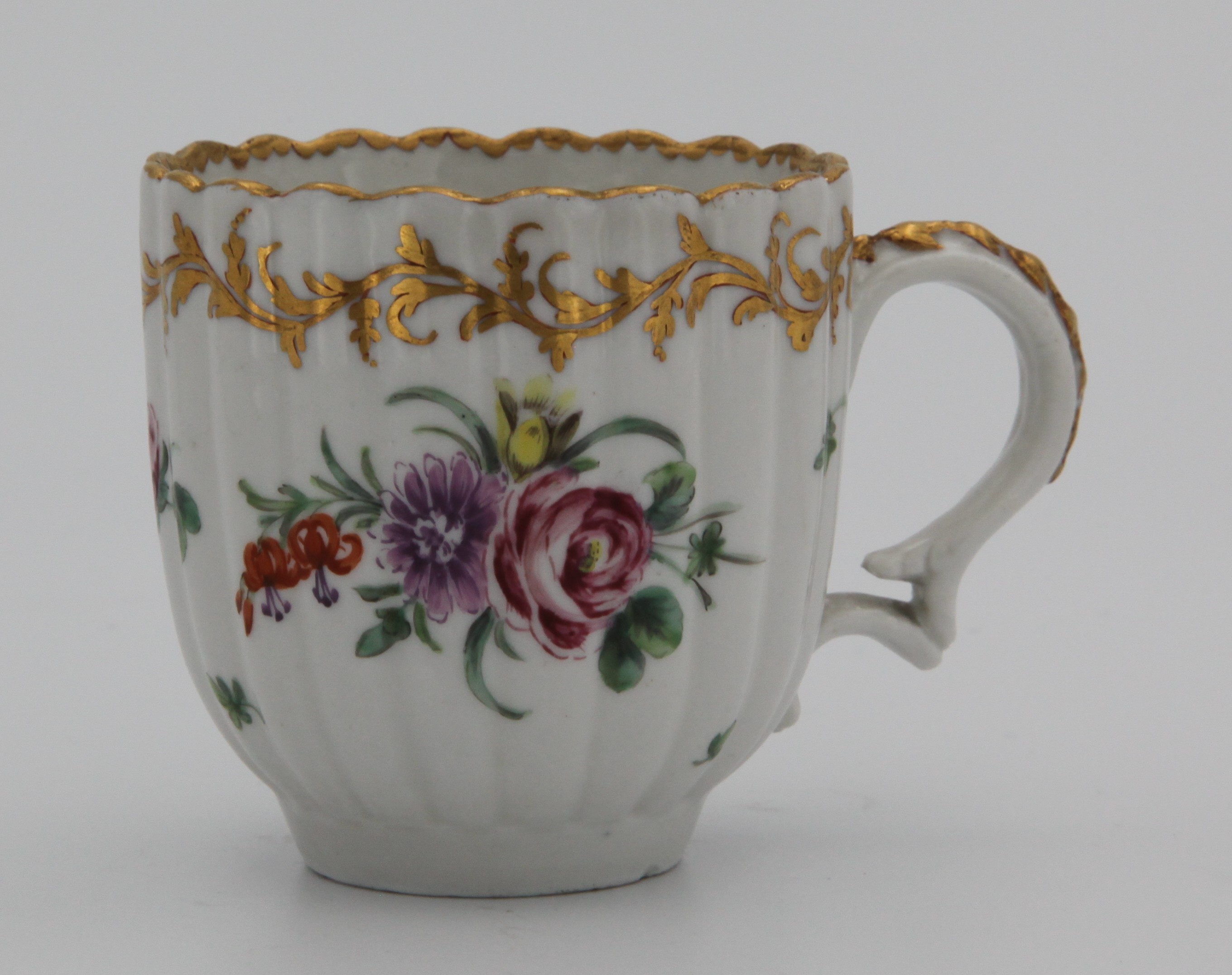 A fine fluted Bristol coffee cup with double scroll handle moulded with harebells and decorated with gilt, painted in enamels with a spray of flowers and scattered leaves and individual flowers, and with an elaborate leafy gilt band, mark blue X1. gilt.
