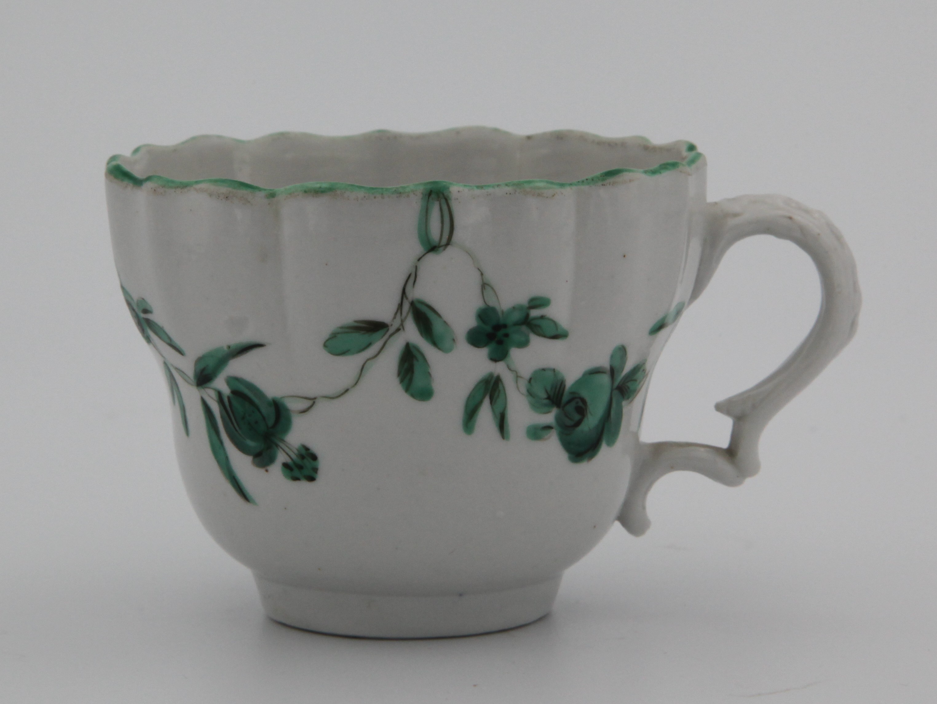 An ogee-shaped Bristol teacup, slightly fluted with moulded double scroll handle, painted in enamels with monochrom green garlands suspended from green looops hanging from a green rim line. Mark blue B