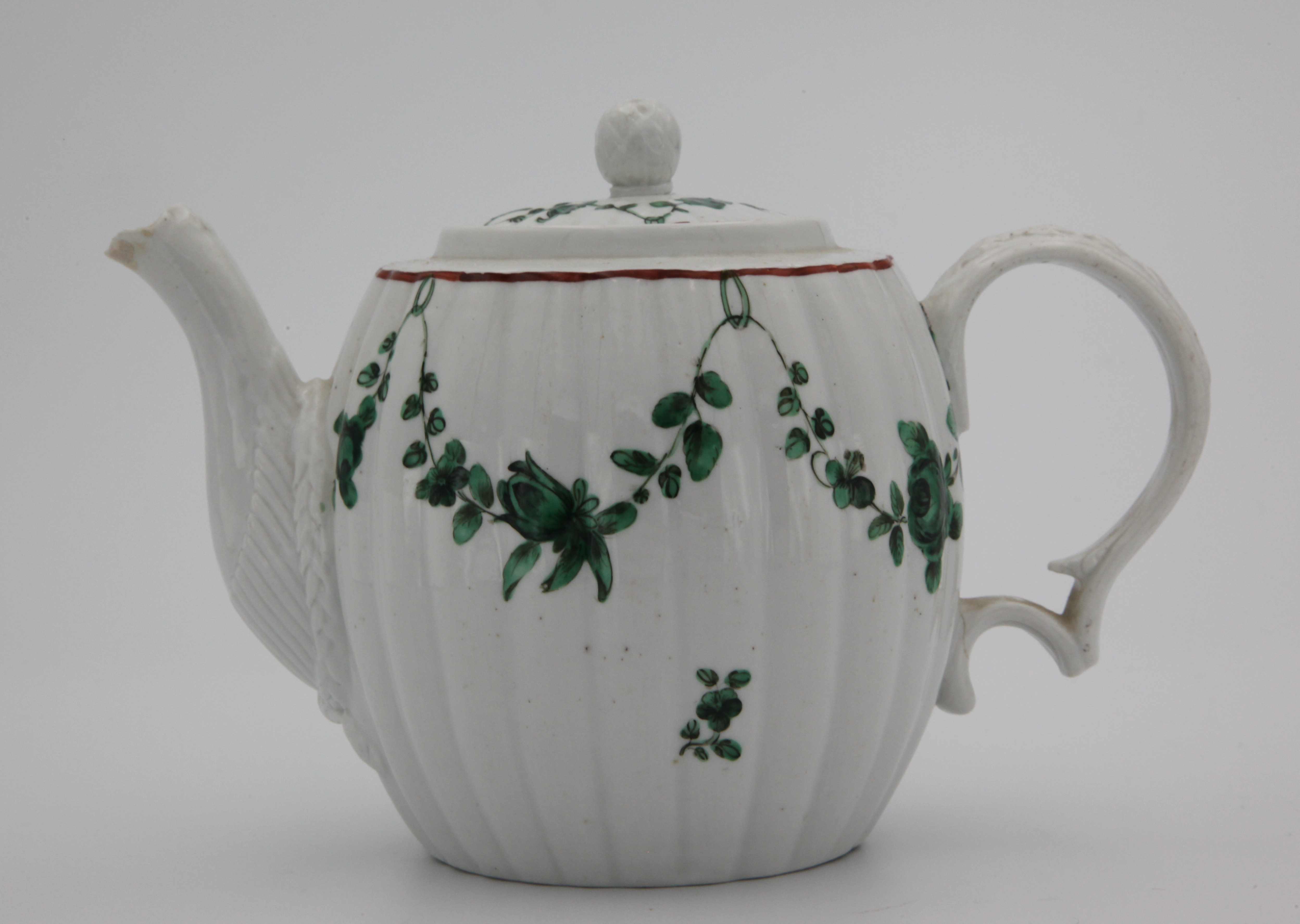 A fluted, barrel-shaped Bristol teapot and cover with ball finial, with harebell moulded handle and decorative moulding around spout, painted in enamels with green monochrome garlands suspended from green loops hanging from an iron red rim line, mark blue X17.