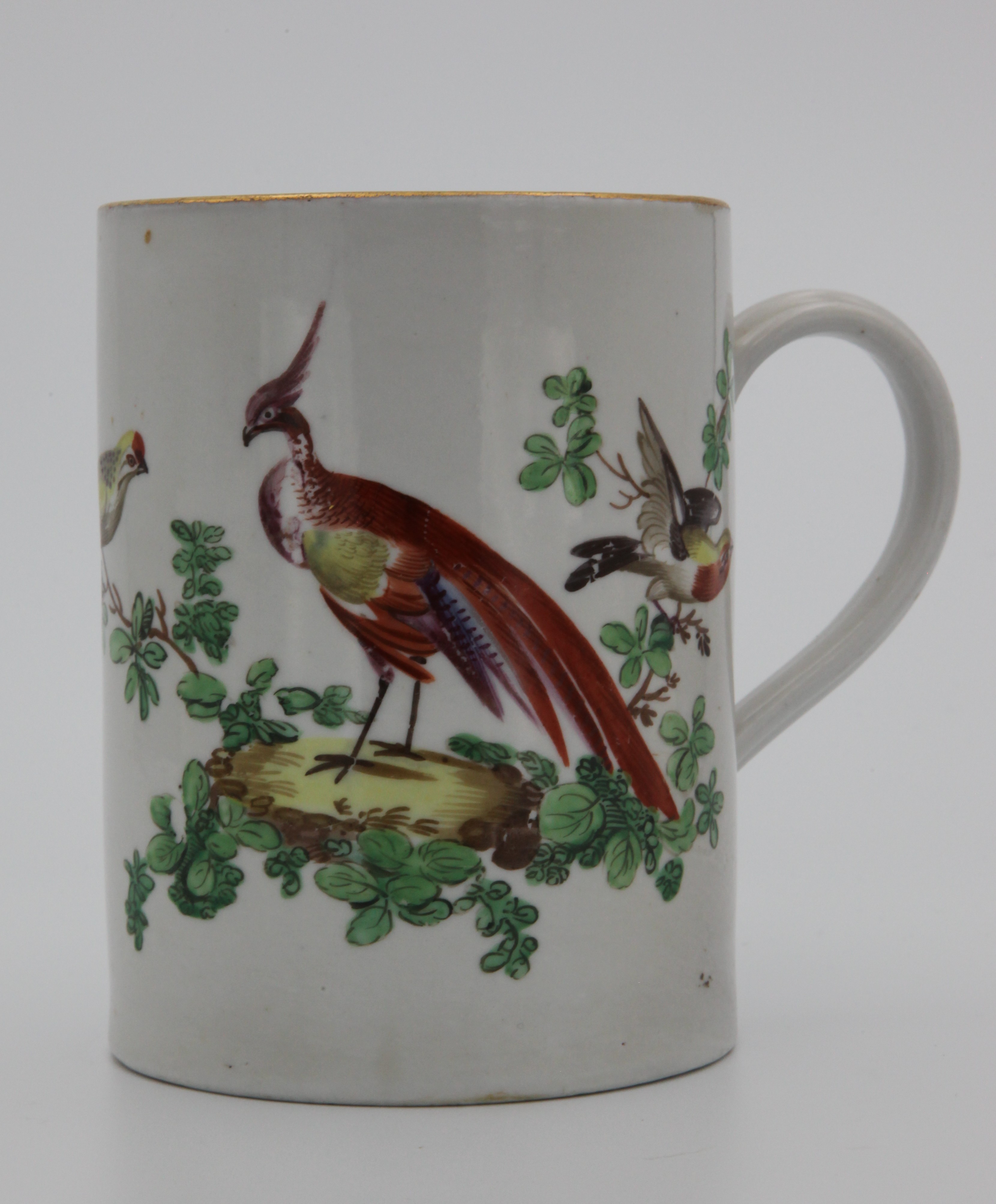 A Bristol large cylindrical mug, with notched loop handle, finely painted in coloured enamels with an exotic bird in a landscape, flanked by naturalistic birds in branches, the reverse painted with two birds in flight, gilt line rim, circa 1775, no mark