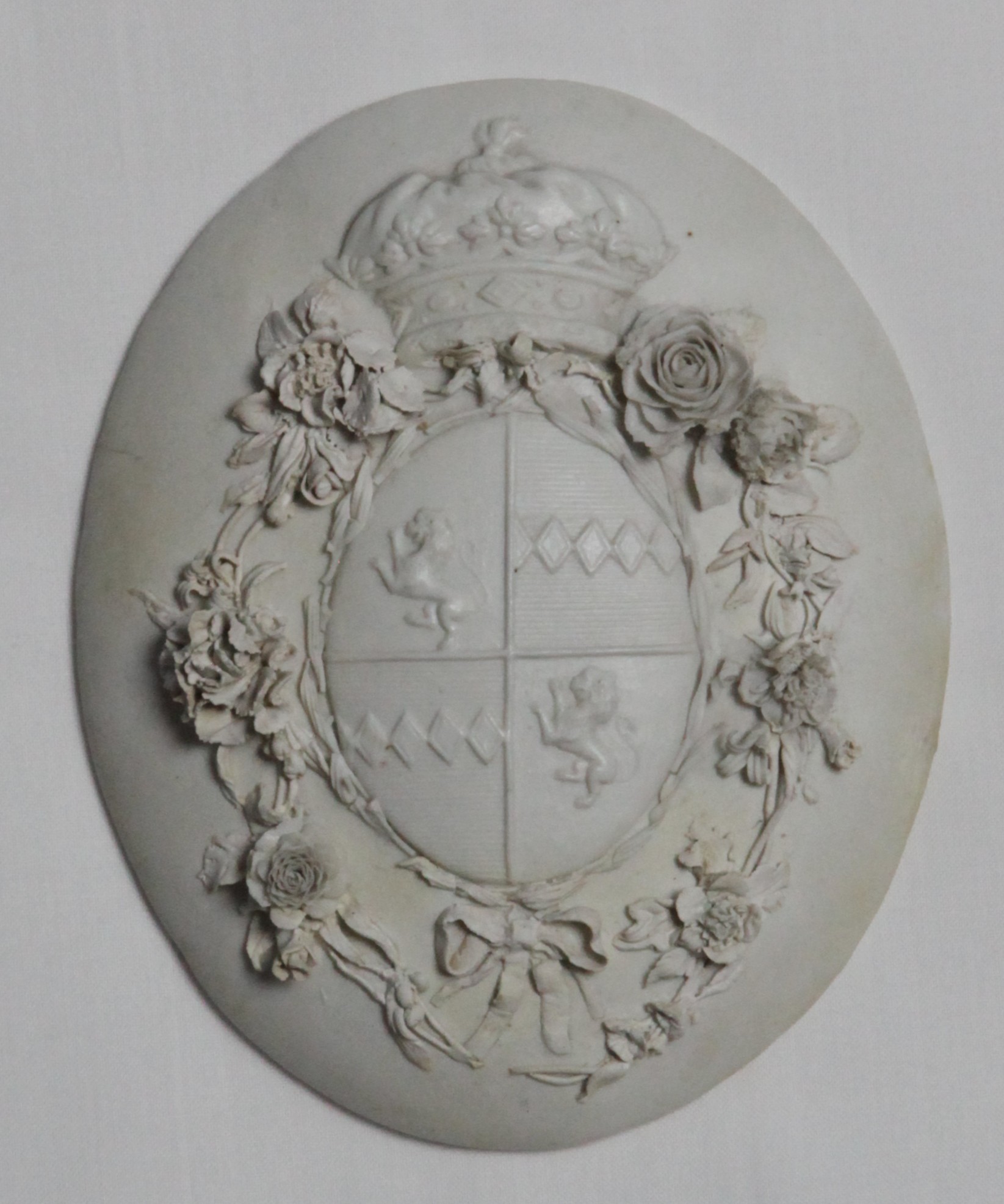 Plaque, from the Plaques service, decorated by No mark, A rare Bristol biscuit porcelain oval plaque, modelled with the arms of Percy beneath a coronet, within an applied ribbon tied laurel garland, and an outer border of applied flowers and leaves, circa 1775 — Plymouth & Bristol porcelain piece 1471