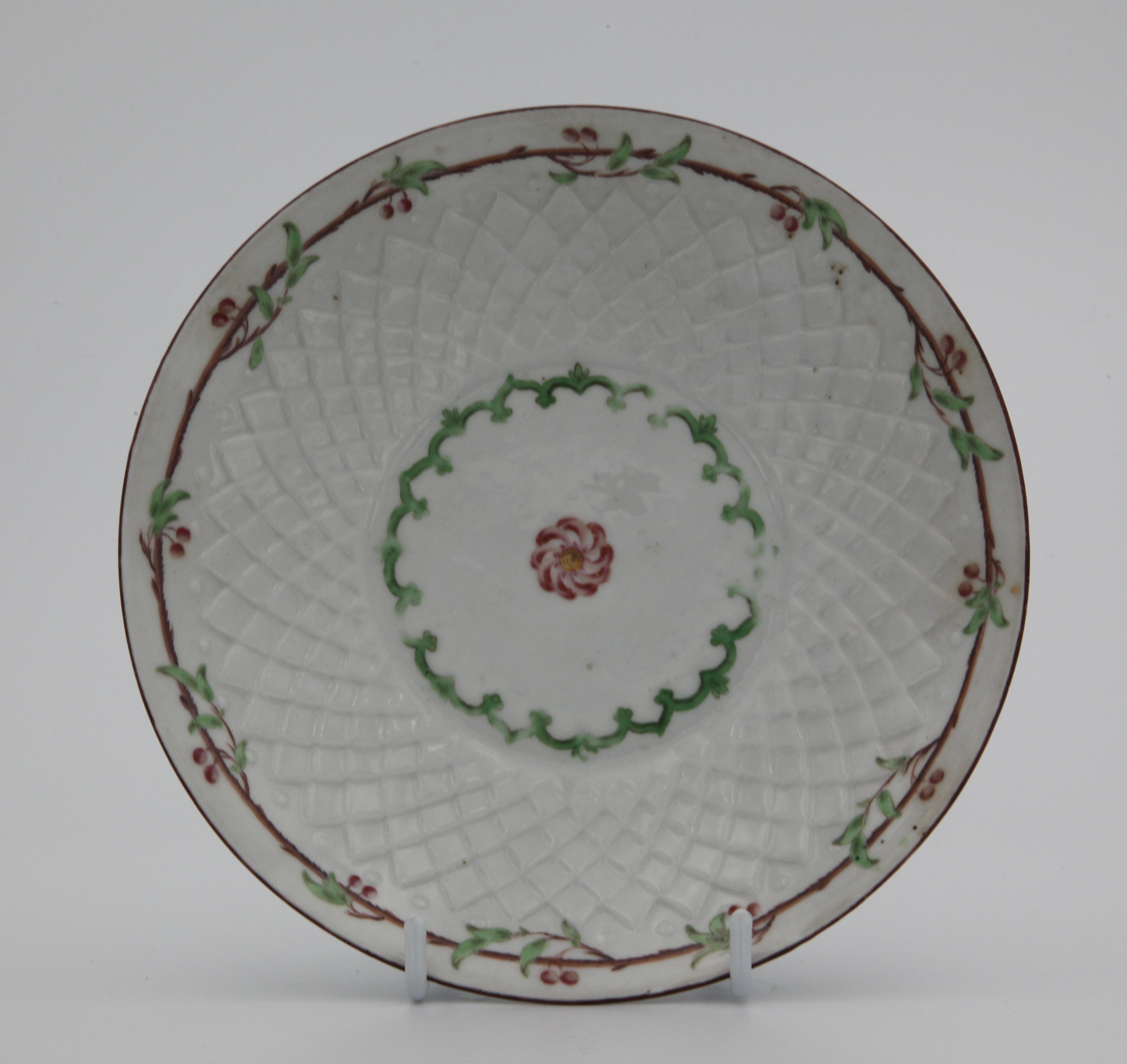 A Bristol pinecone moulded saucer, painted in enamels with a central puce and yellow floral roundel, surrounded by a green patterned band and all surrounded by a green and brown cherry tree branch motif under a brown rim line.