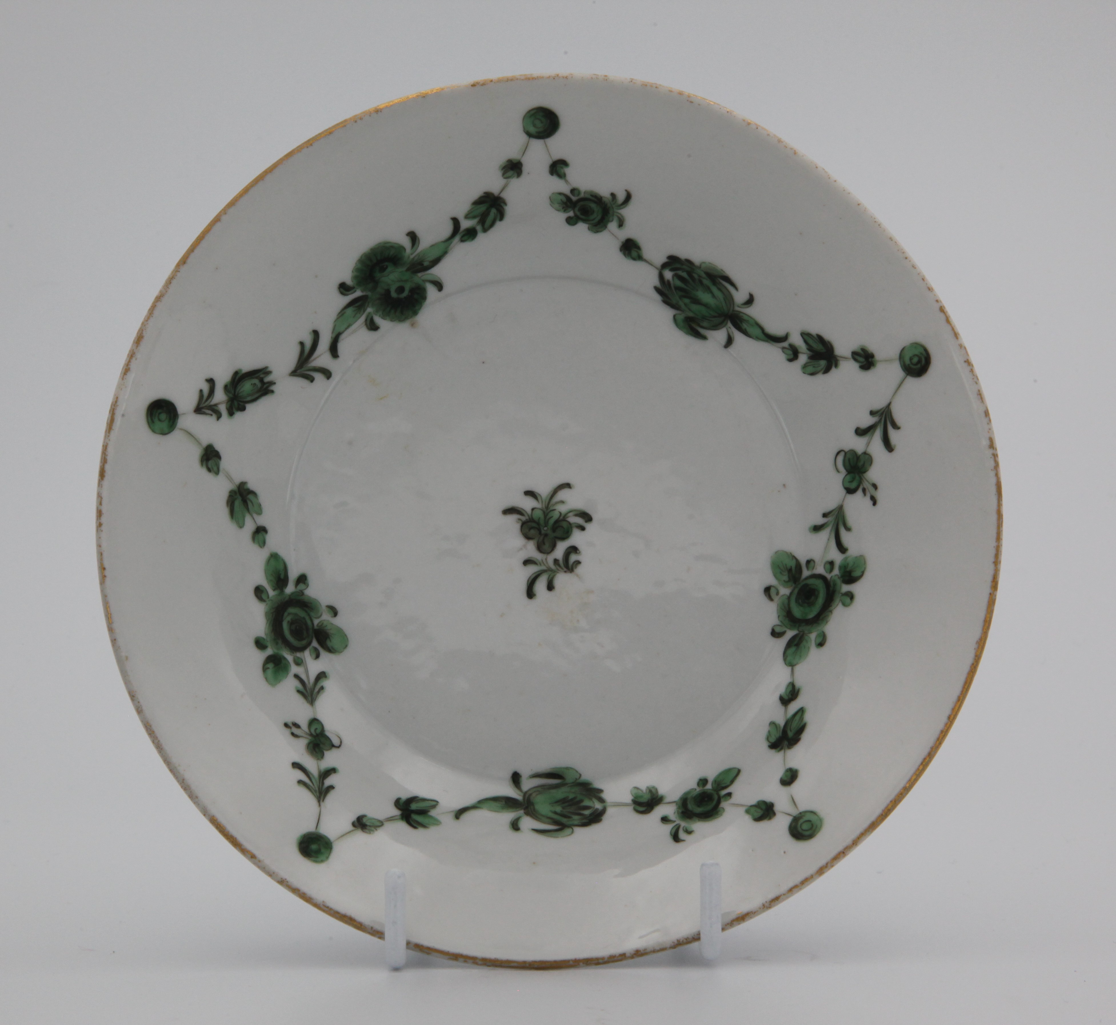A Bristol deep-sided saucer painted in enamels with monochrome green garlands of flowers and leaves suspended from green roundels below a gilt rim line