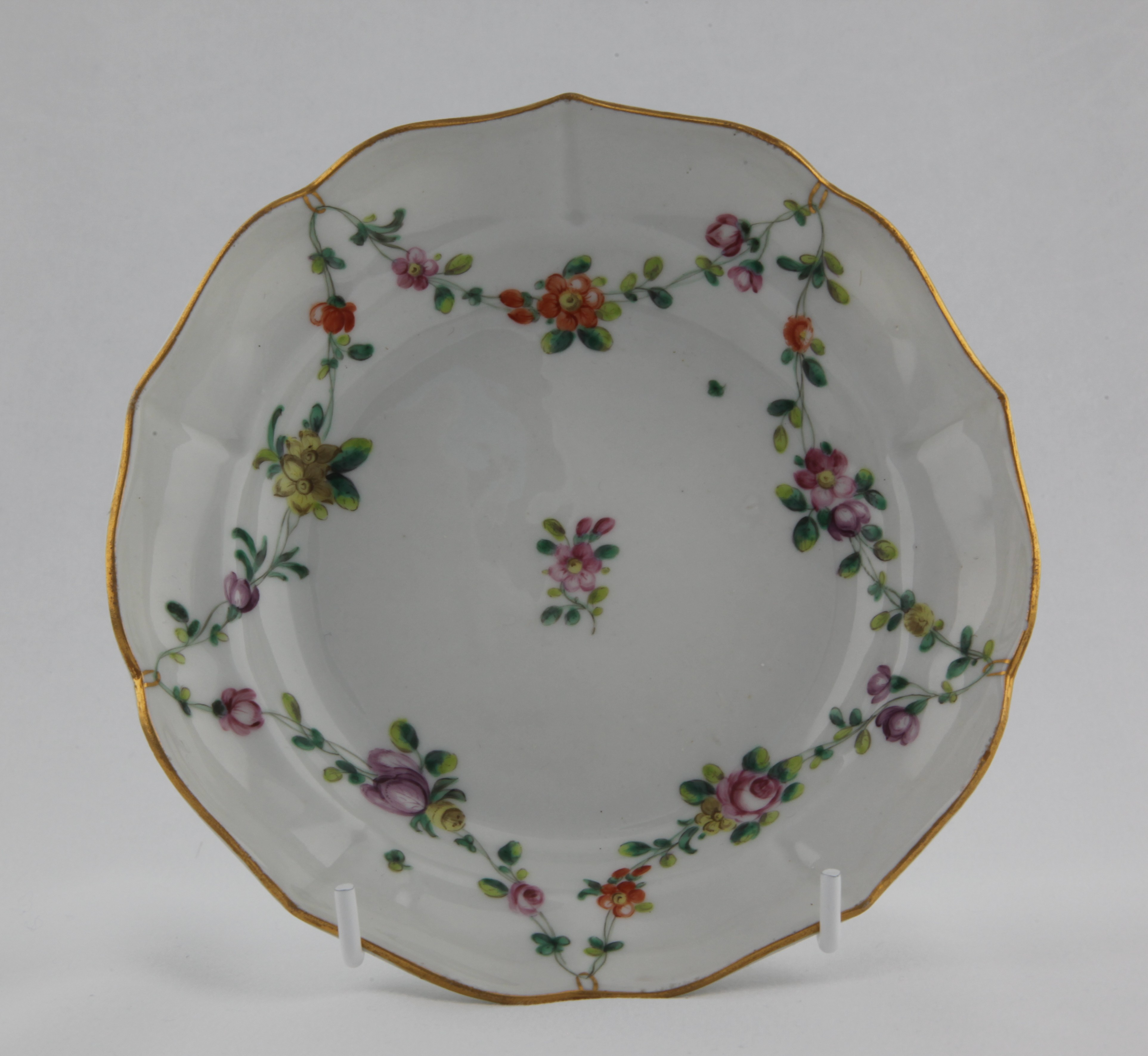 Saucer, from the Gilt loop garland service, decorated by No mark, A Bristol saucer, ogee-shaped and mildly lobed, painted in enamels with garlands of colourful flowers and leaves suspended from gilt loops hanging from a gilt rim line — Plymouth & Bristol porcelain piece 1480