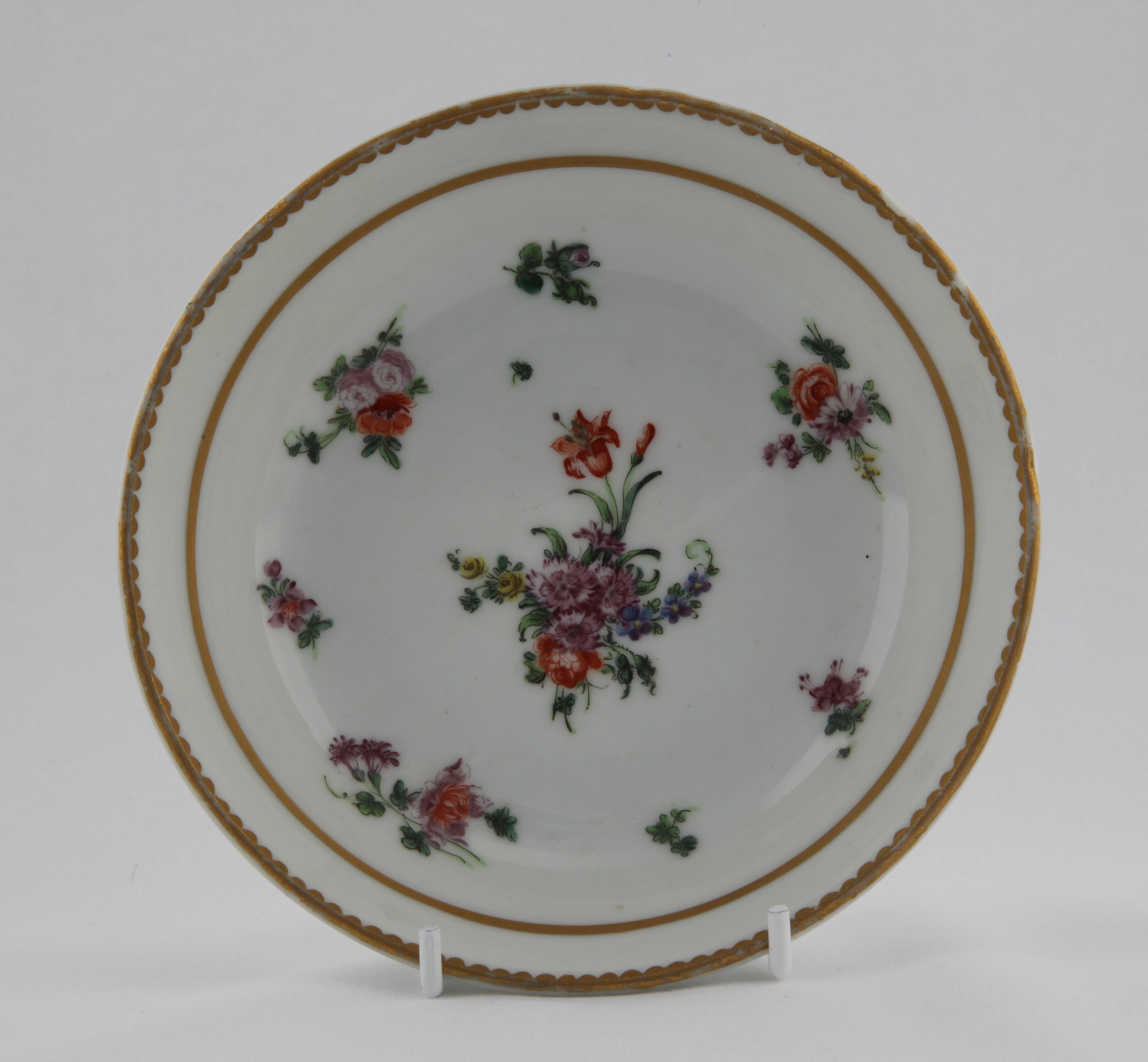 Saucer, from the Thick gold line service, decorated by No mark, A deep Bristol saucer of ogee shape, painted in enamels with a prominent central spray and scattered flowers surrounded by a thick gilt line all within a gilt dentil rim line — Plymouth & Bristol porcelain piece 1481