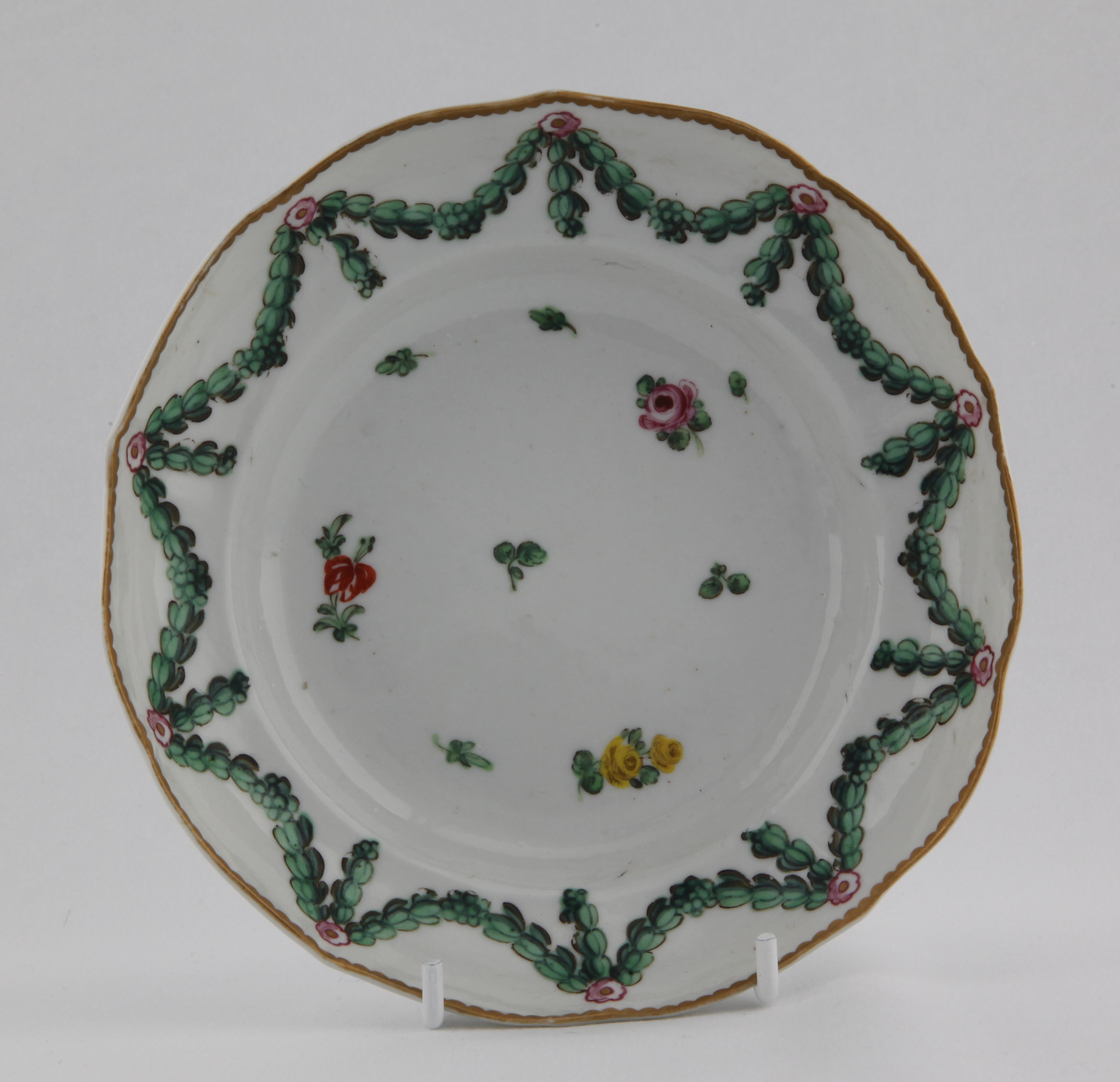 A Bristol ogee shaped chocolate cup saucer painted with scattered sprigs under green acanthus garlands hanging from rose roundels under a gilt dentil rim. Mark: 4. in gold