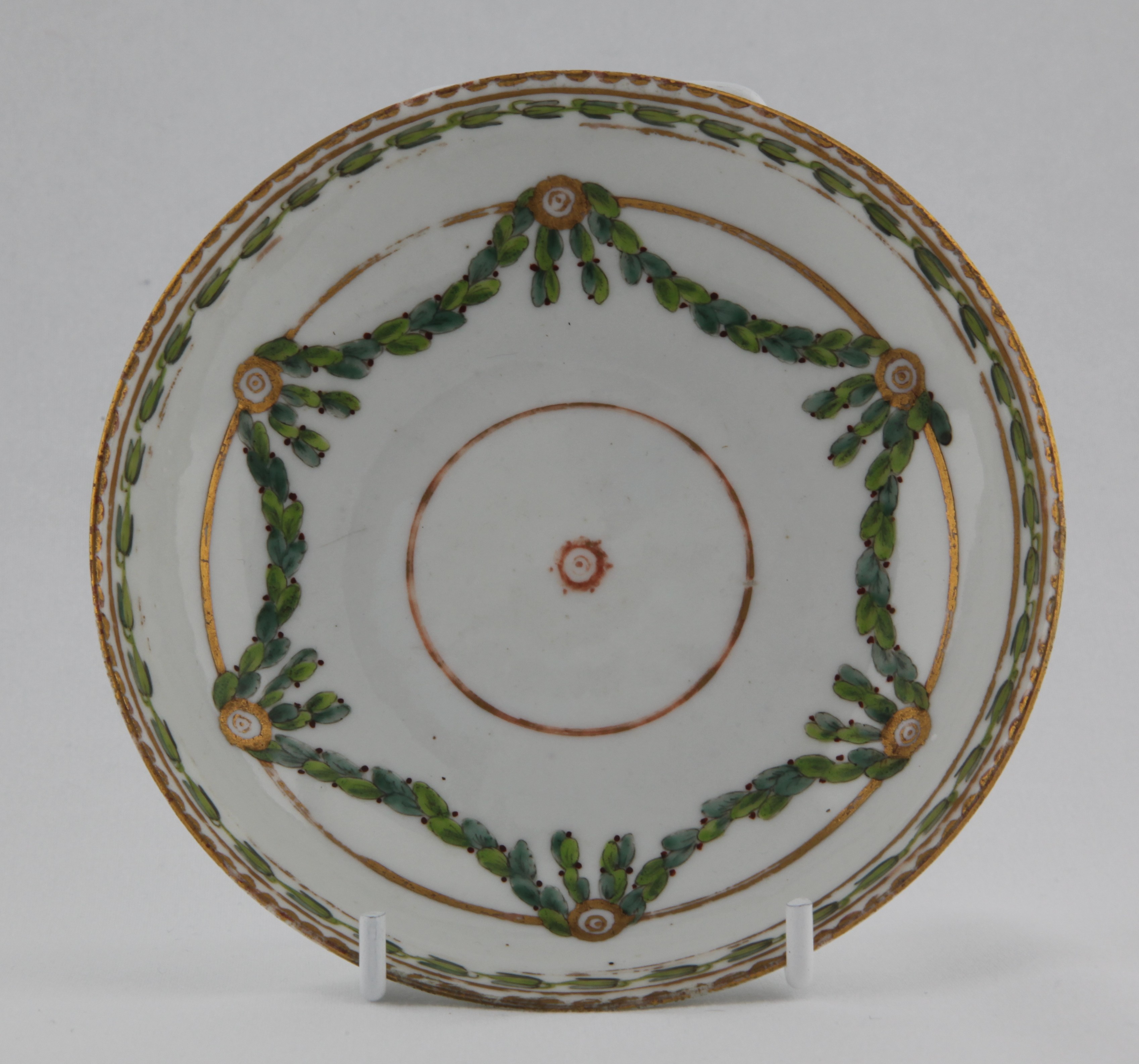 Saucer, from the Laurel swag service, decorated by No mark, A Bristol saucer of rounded shape with laurel swags suspended from gilt roundels handing on a gilt line surrounded by a harebell band under a gilt dentil rim — Plymouth & Bristol porcelain piece 1485