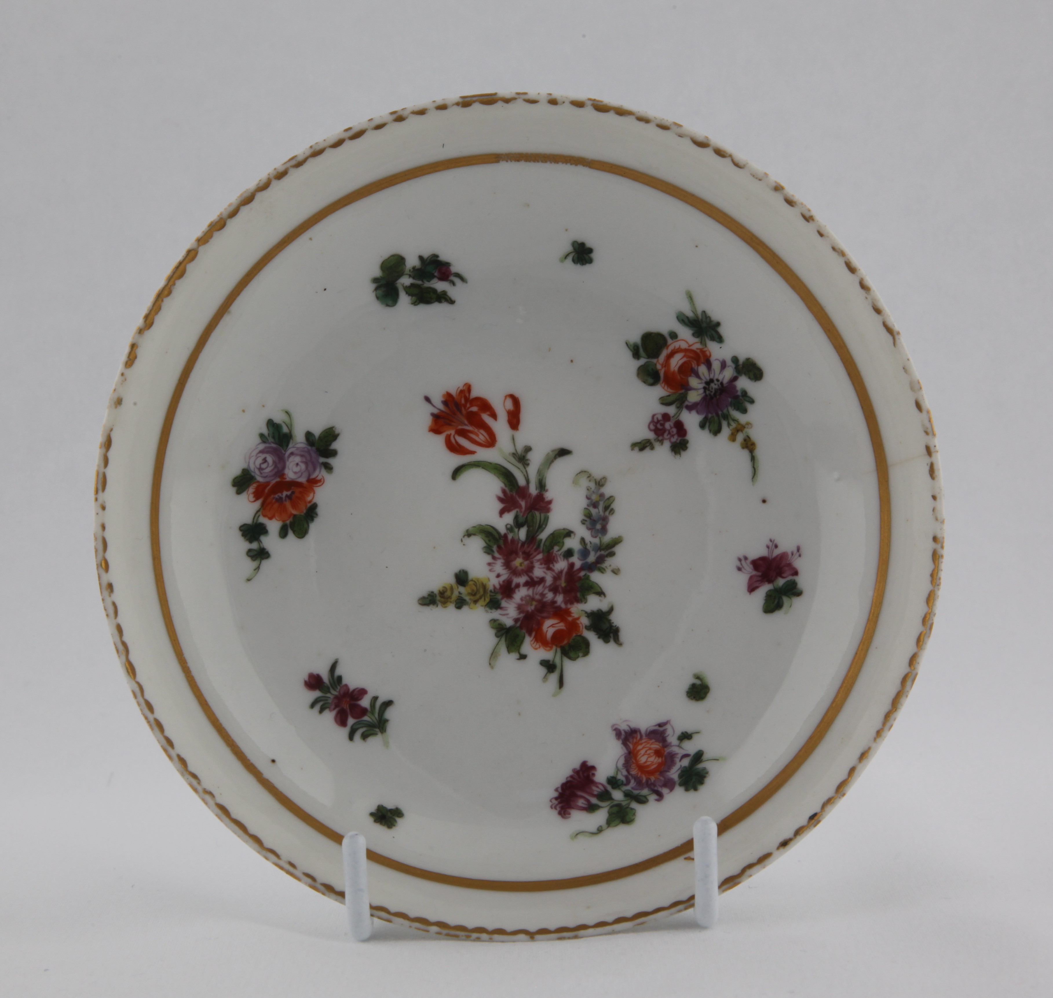 Saucer, from the Thick gold line service, decorated by No mark, A Bristol saucer of rounded shape, painted in enamels with a prominent central spray and scattered flowers surrounded by a thick gilt line all within a gilt dentil rim line — Plymouth & Bristol porcelain piece 1486