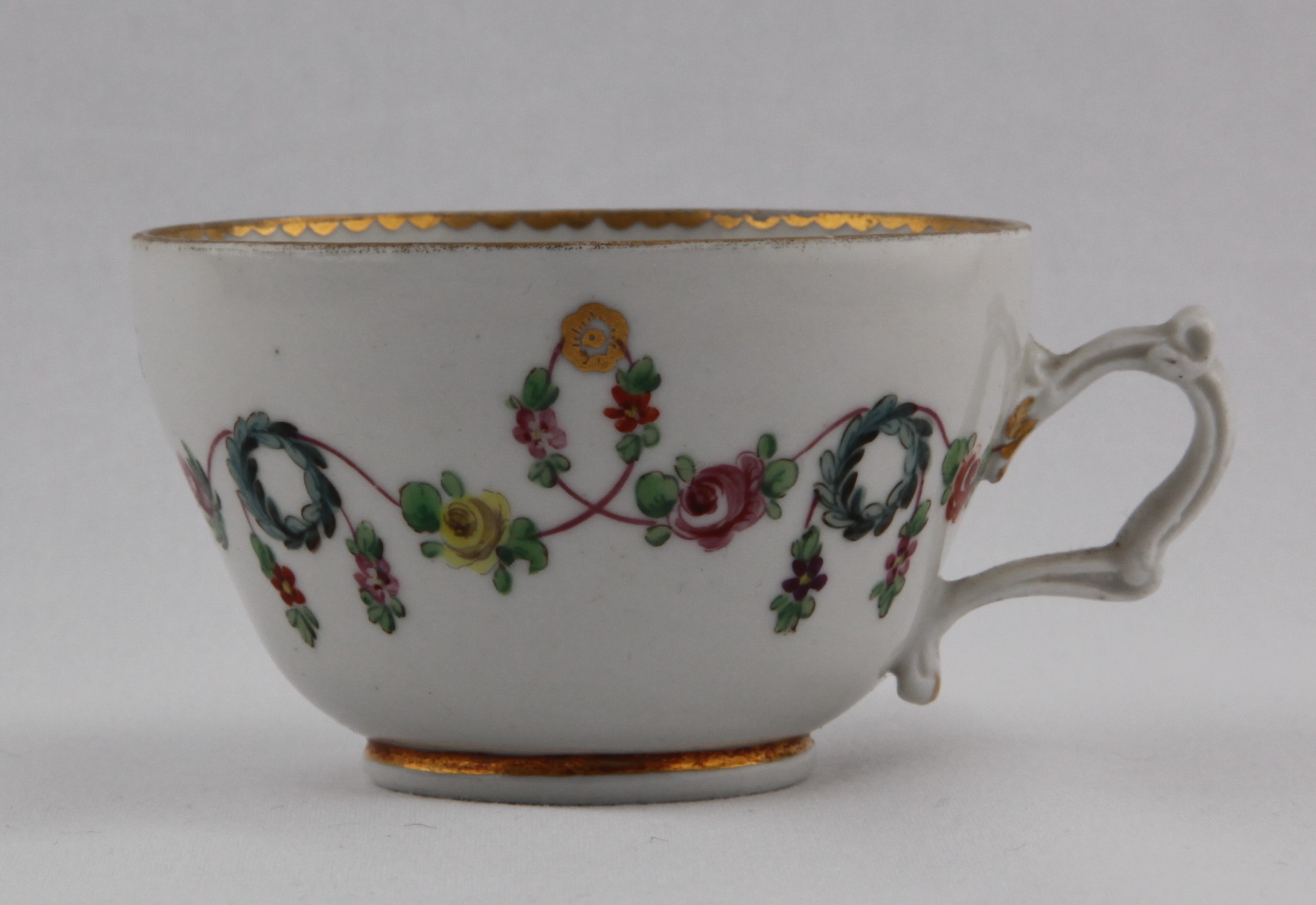 Cup, from the Blue wreath service, decorated by 1, A very fine Bristol tea cup, slightly ogee, with elaborate moulded (but wonky) handle, painted with colourful swags of leaves and flowers on a pink line, suspended from gilt roundels and looping over blue wreaths, with gilt dentil rim and central rose in base of bowl — Plymouth & Bristol porcelain piece 1491