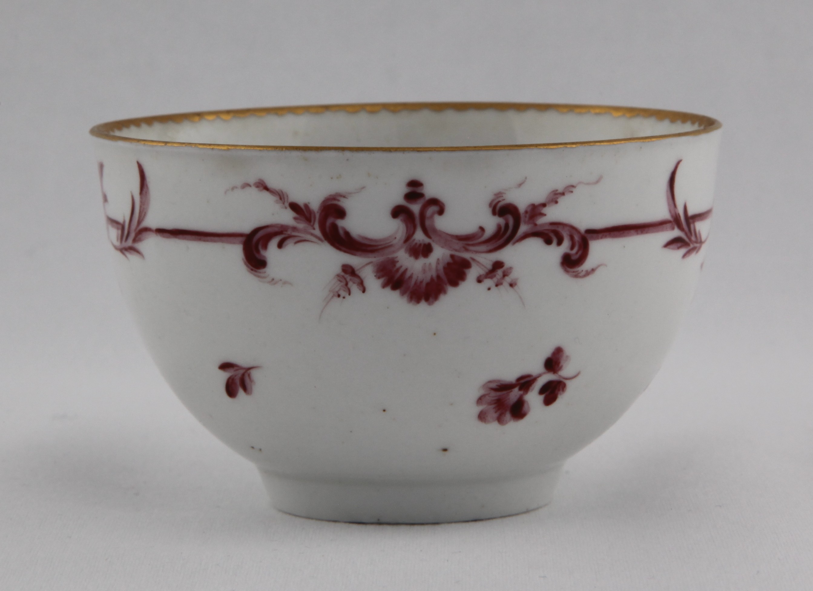 Tea bowl, from the Puce monochrome service, decorated by 6, A Bristol tea bowl, of rounded shape, painted with monochrome puce scroll band with scattered flowers under gilt dentil rim — Plymouth & Bristol porcelain piece 1496