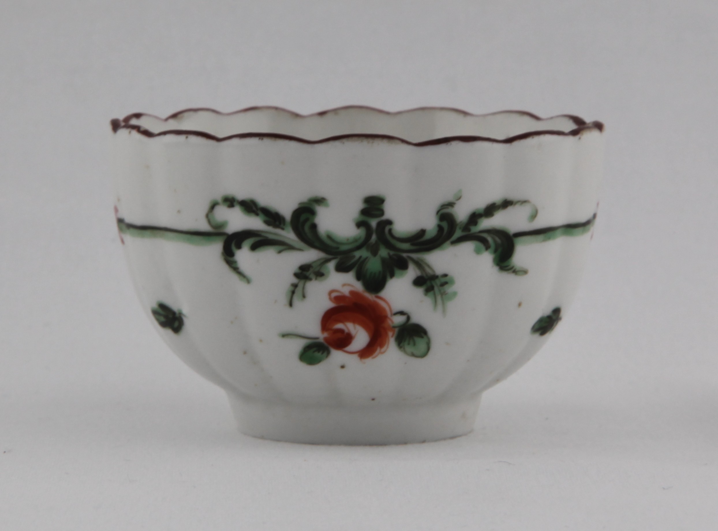 Tea bowl, from the Green scroll band service, decorated by 6, A fluted Bristol tea bowl painted in enamels with green scroll bands supporting flowers and with scattered leaves under an iron red rim line — Plymouth & Bristol porcelain piece 1498