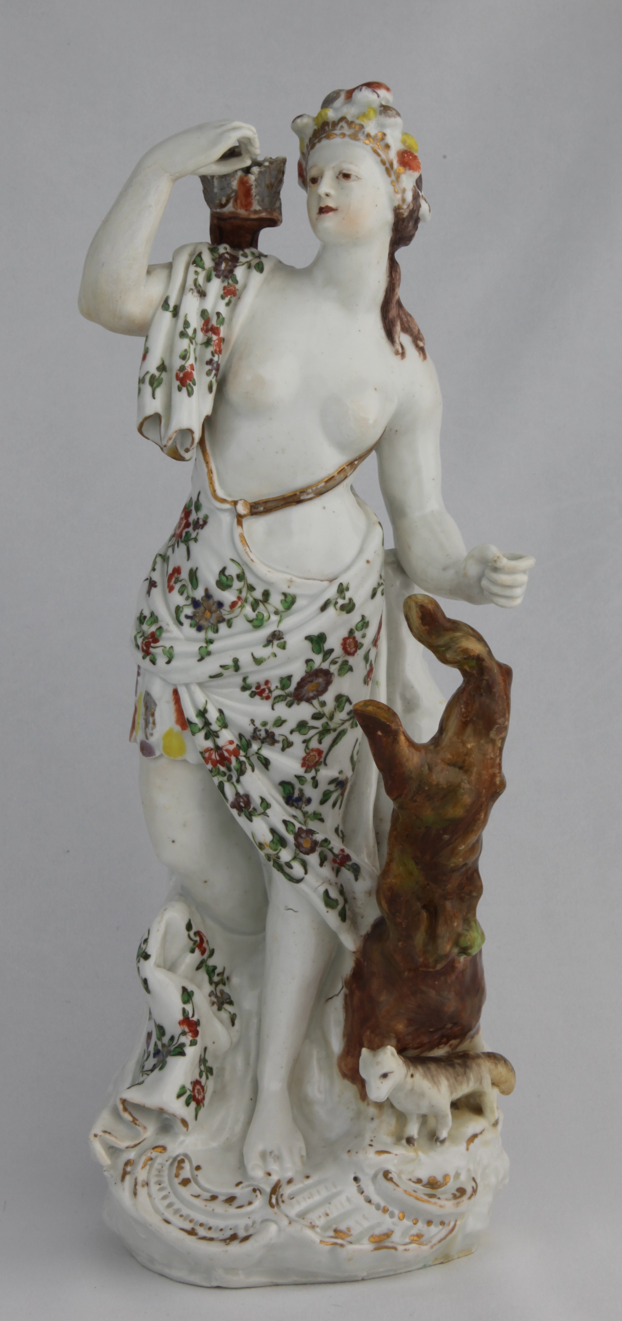 Figure, from the Continents service, decorated by No mark, A Plymouth (William Cookworthy) figure of America, circa 1768-70 From a set of the Four Continents, modelled as a woman wearing a feathered headdress and finely painted and gilt drapery over a feather skirt, her right hand reaching for an arrow in the quiver over her shoulder, her left hand by a tree stump, a small prairie dog at her feet, on a scroll-edged rocky base, 33.8cm high — Plymouth & Bristol porcelain piece 1504