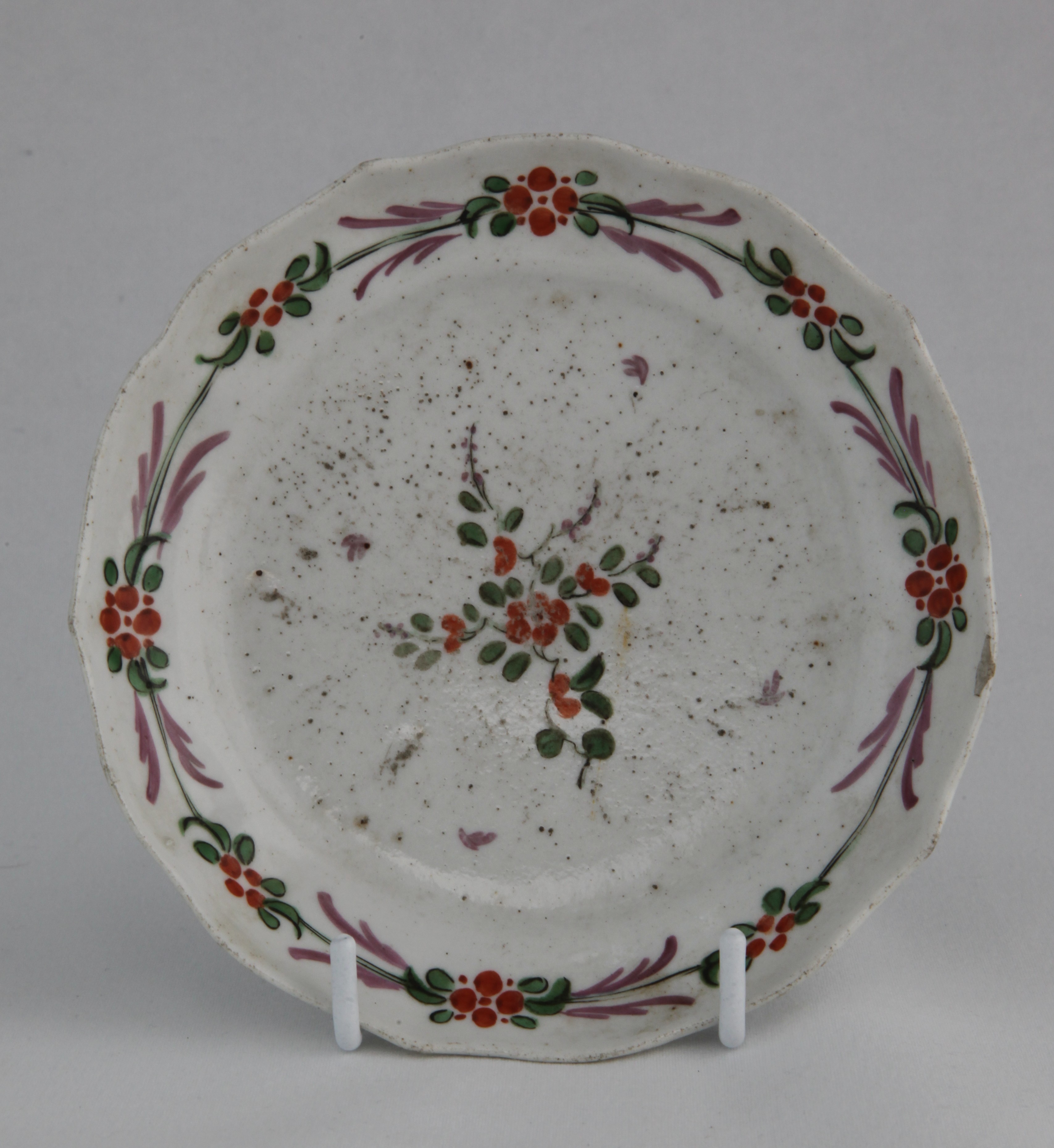 An extremely rare Plymouth ogee-form teabowl saucer unusually polychrome painted with simple green, orange and puce floral sprays under a similarly coloured band.