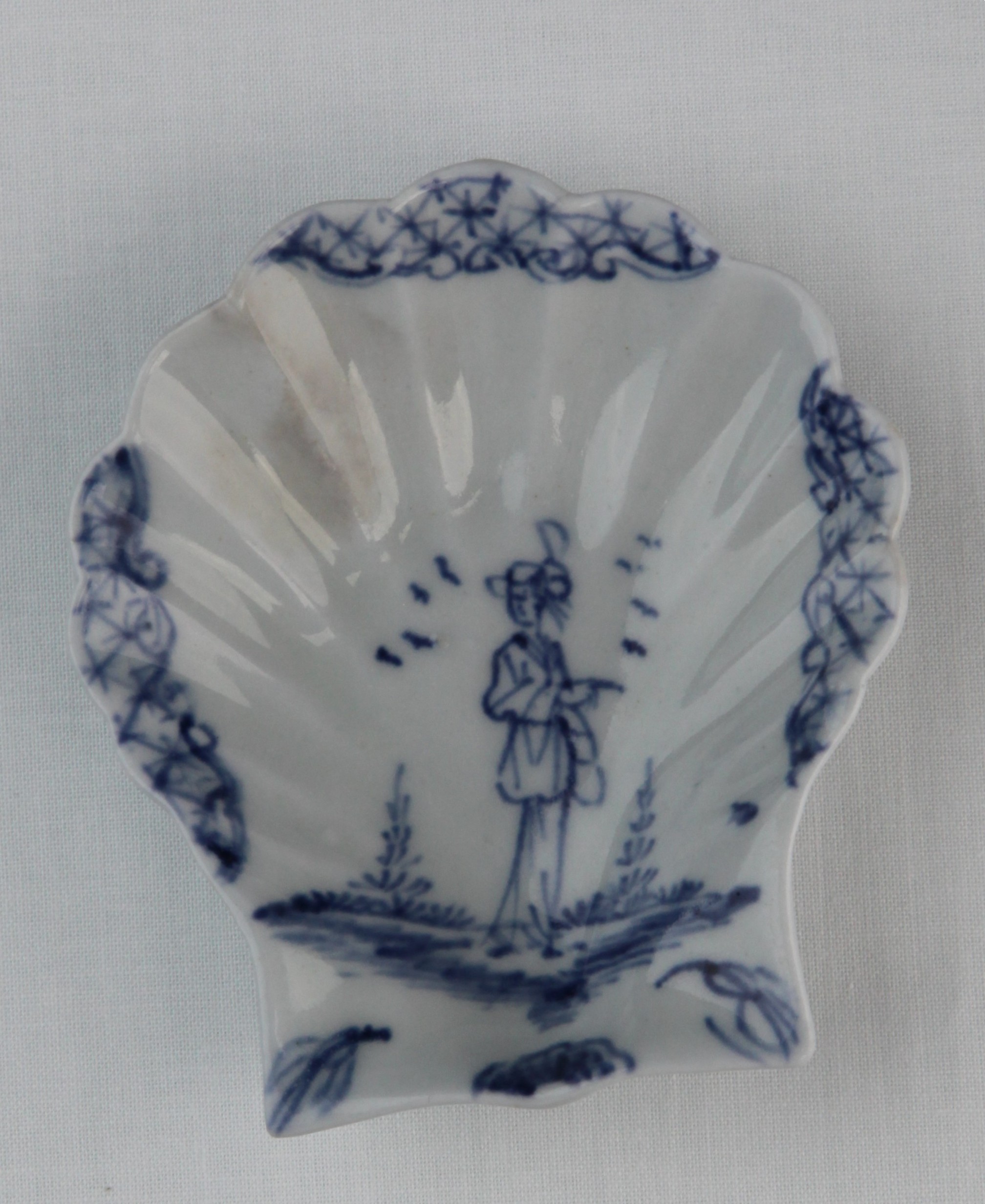 A Lund's Bristol scallop shell pickle dish, circa 1750, of small size and simply moulded, painted in blue with a cartoon-like 'Long Eliza' figure pointing, surrounded by birds in flight, diaper panels edged with scrollwork around the rim, two leaves and a shell at the base, 9.2cm high