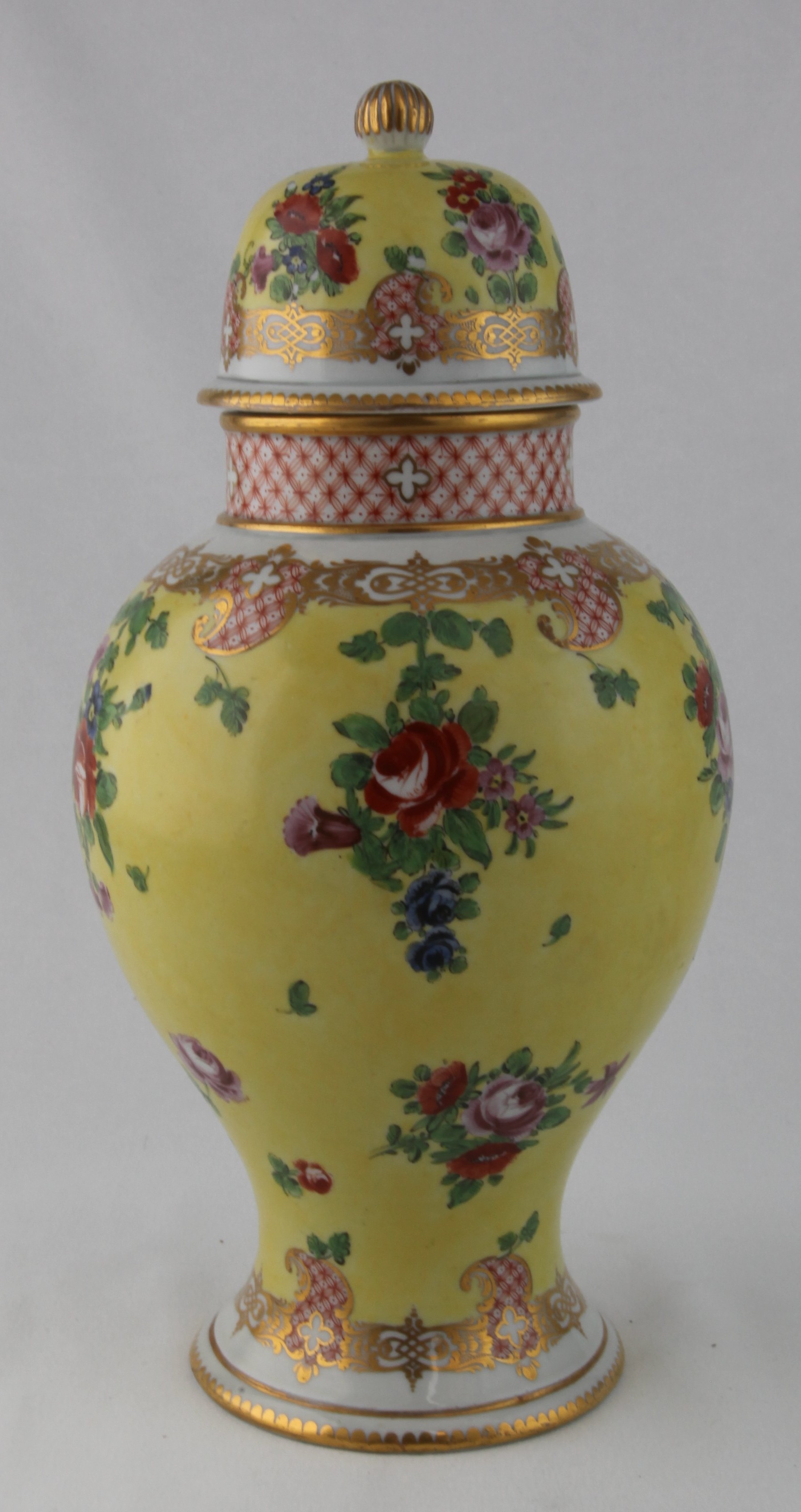 One of a rare pair of Champion's Bristol vases and covers, circa 1772-75, of baluster form, painted with colourful sprays and scattered sprigs of flowers including roses in red and puce, all on a bright yellow ground, within formal diaper and scrollwork borders in red and gold, the necks with diaper bands, the high domed covers similarly decorated, with gilt dentil rims and gilt fluted finials