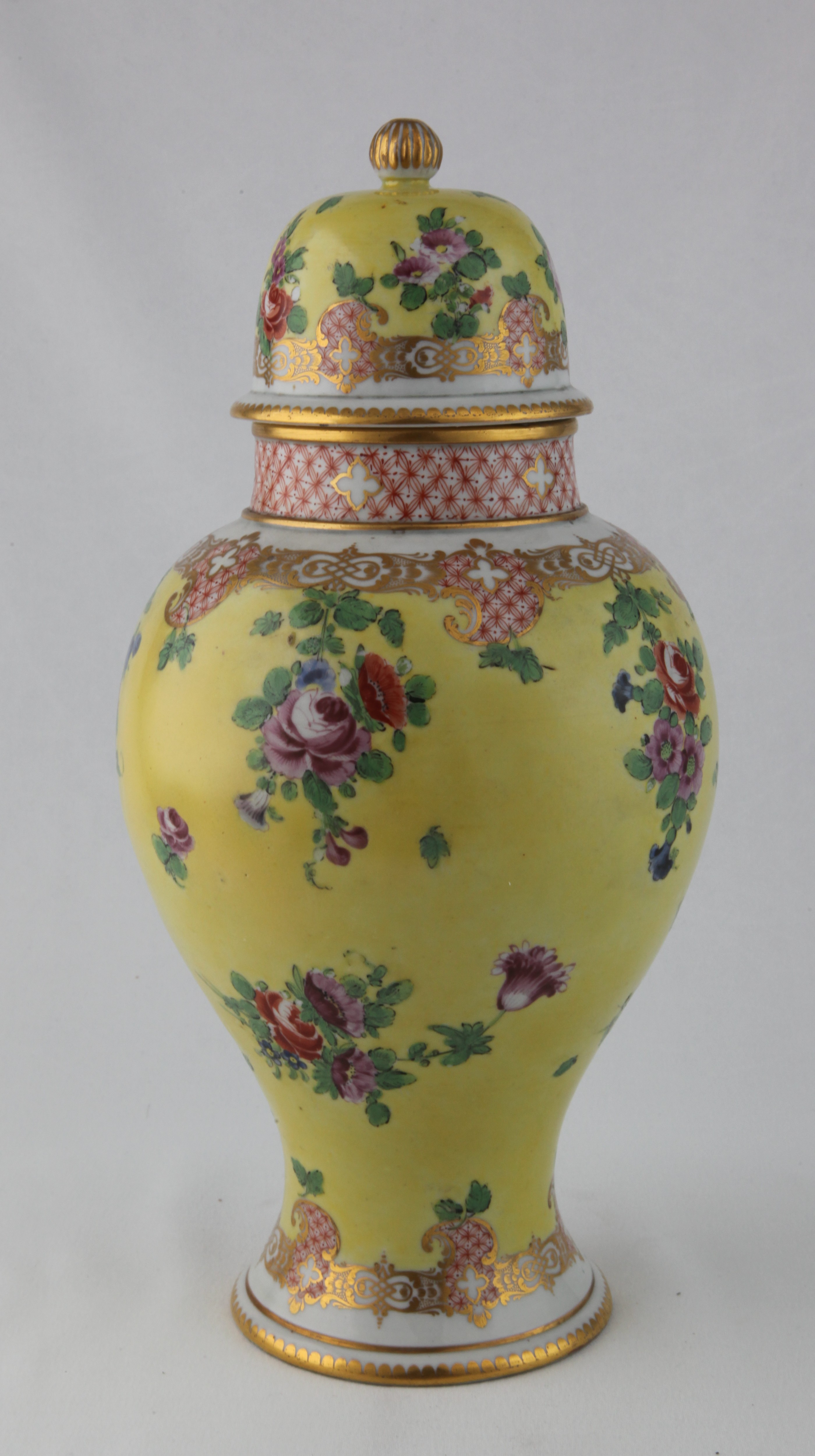 One of a rare pair of Champion's Bristol vases and covers, circa 1772-75, of baluster form, painted with colourful sprays and scattered sprigs of flowers including roses in red and puce, all on a bright yellow ground, within formal diaper and scrollwork borders in red and gold, the necks with diaper bands, the high domed covers similarly decorated, with gilt dentil rims and gilt fluted finials