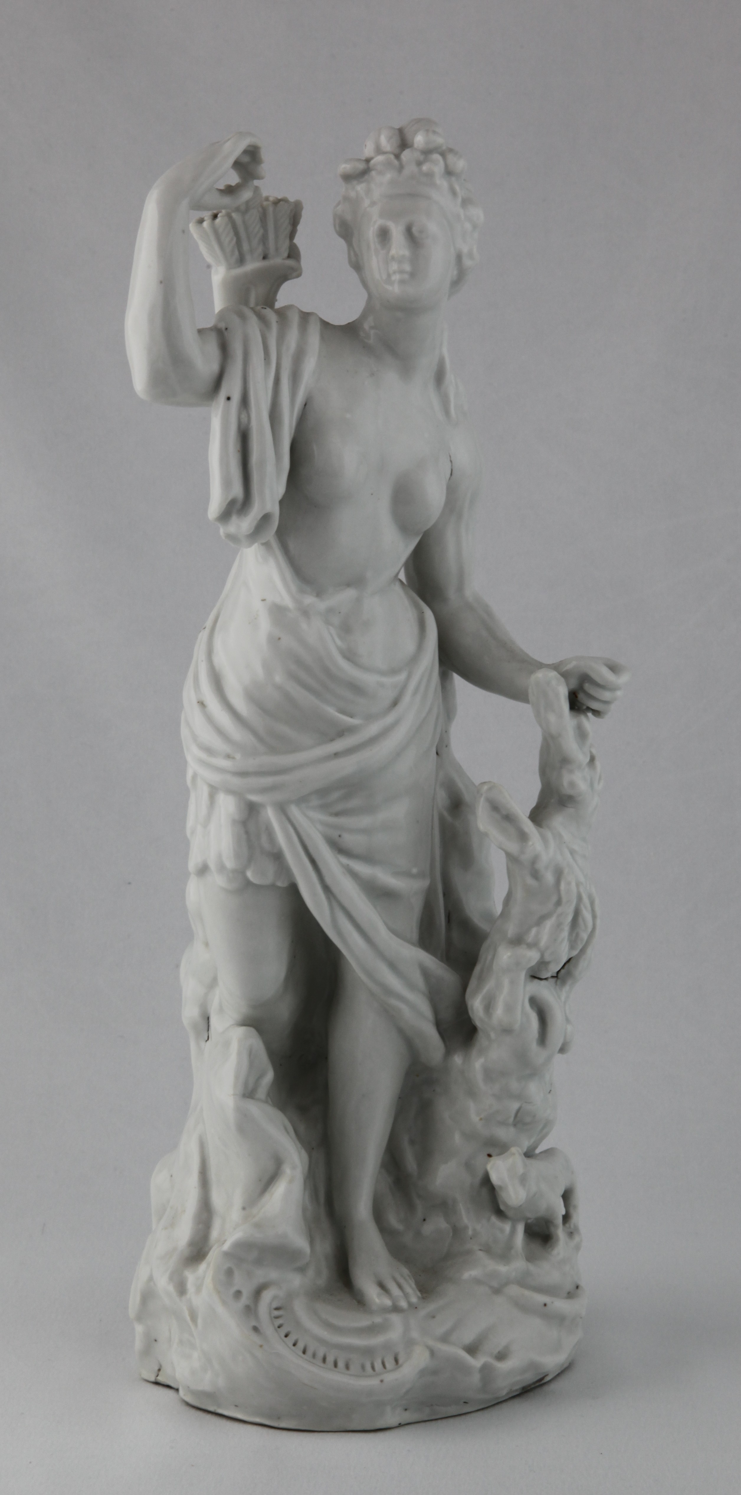 America, from a rare set of four Plymouth figures of the Continents, in the white, each represented by a standing young woman; America with feathered headdress and tunic, drawing an arrow from a quiver, a dog at her feet, Asia holding a censer, a camel at her side, Africa with a crocodile and a lion at her feet, and Europe holding a book and an artist’s palette, a horse, cannon and cuirass at her feet, each on scroll moulded mound base, circa 1768-70, no marks