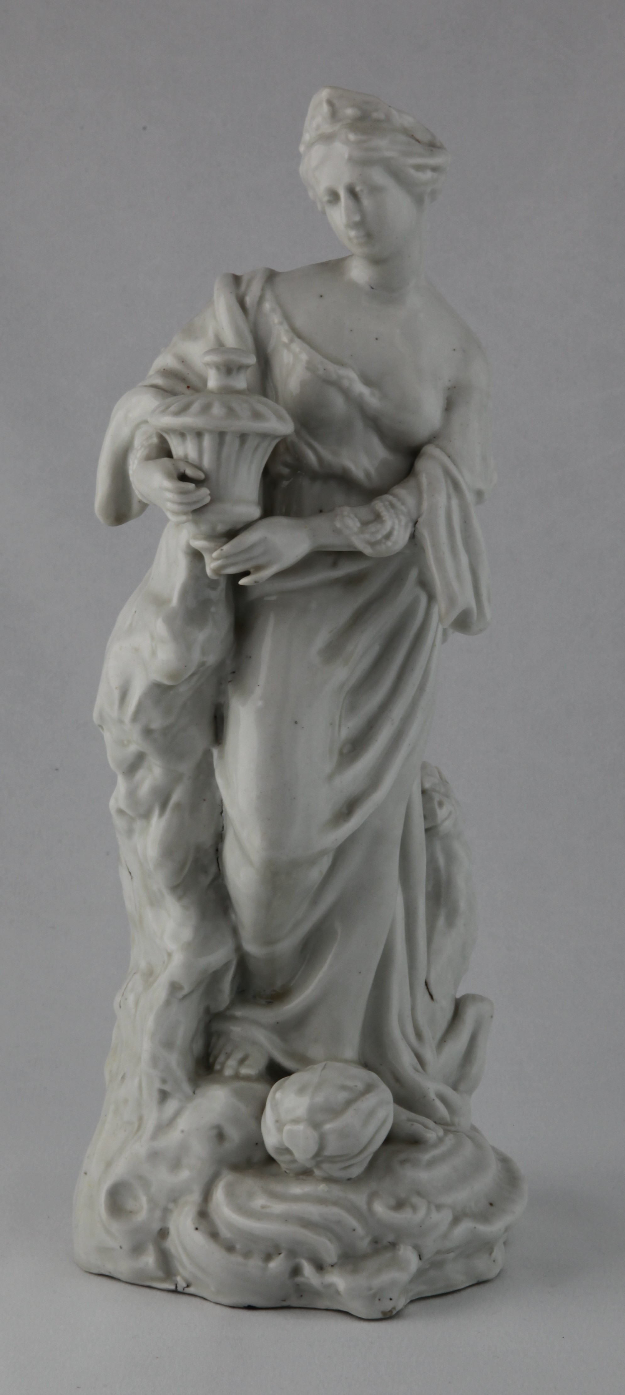 Asia, from a rare set of four Plymouth figures of the Continents, in the white, each represented by a standing young woman; America with feathered headdress and tunic, drawing an arrow from a quiver, a dog at her feet, Asia holding a censer, a camel at her side, Africa with a crocodile and a lion at her feet, and Europe holding a book and an artist’s palette, a horse, cannon and cuirass at her feet, each on scroll moulded mound base, circa 1768-70, no marks