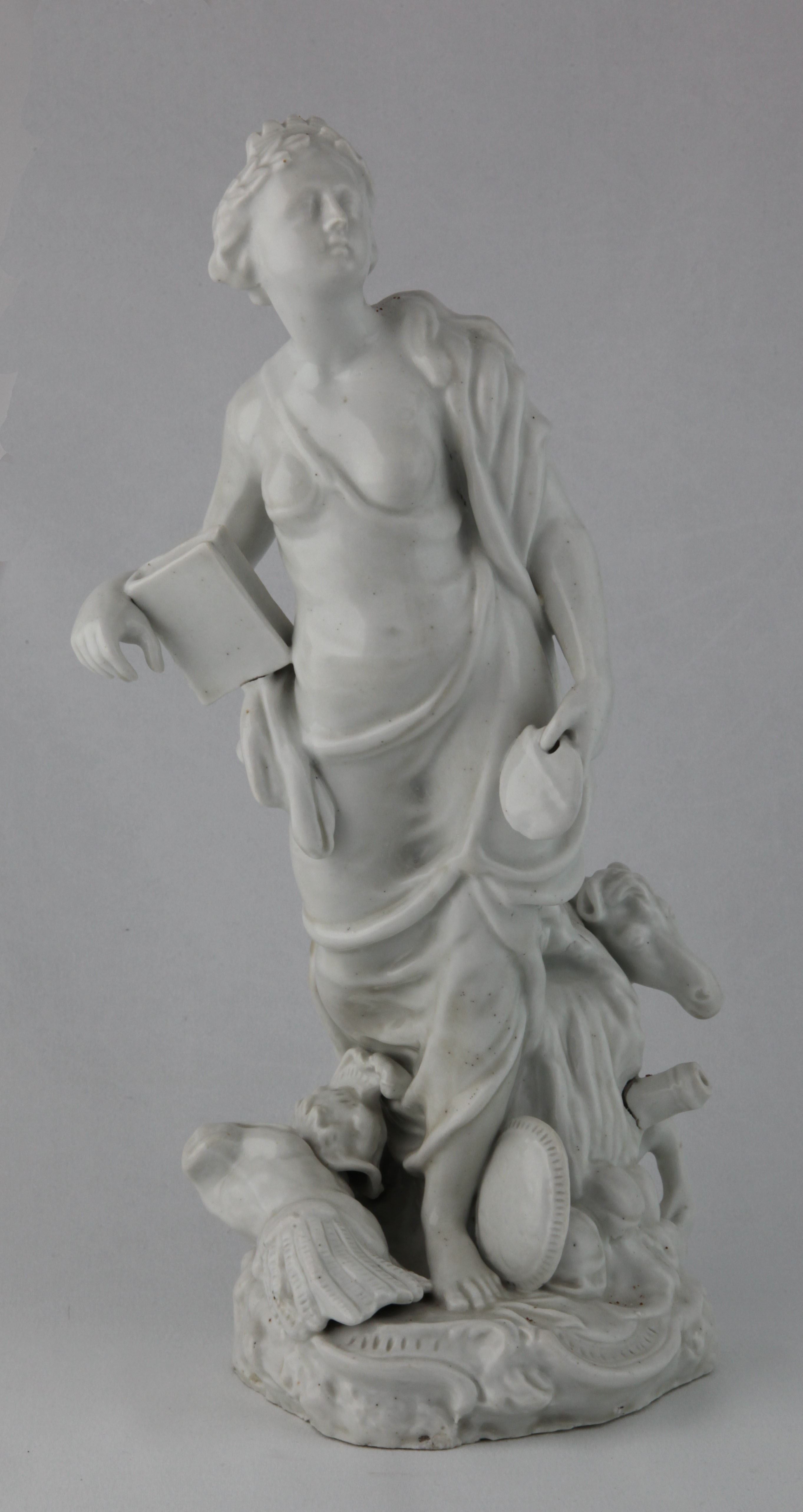 Europe, from a rare set of four Plymouth figures of the Continents, in the white, each represented by a standing young woman; America with feathered headdress and tunic, drawing an arrow from a quiver, a dog at her feet, Asia holding a censer, a camel at her side, Africa with a crocodile and a lion at her feet, and Europe holding a book and an artist’s palette, a horse, cannon and cuirass at her feet, each on scroll moulded mound base, circa 1768-70, no marks