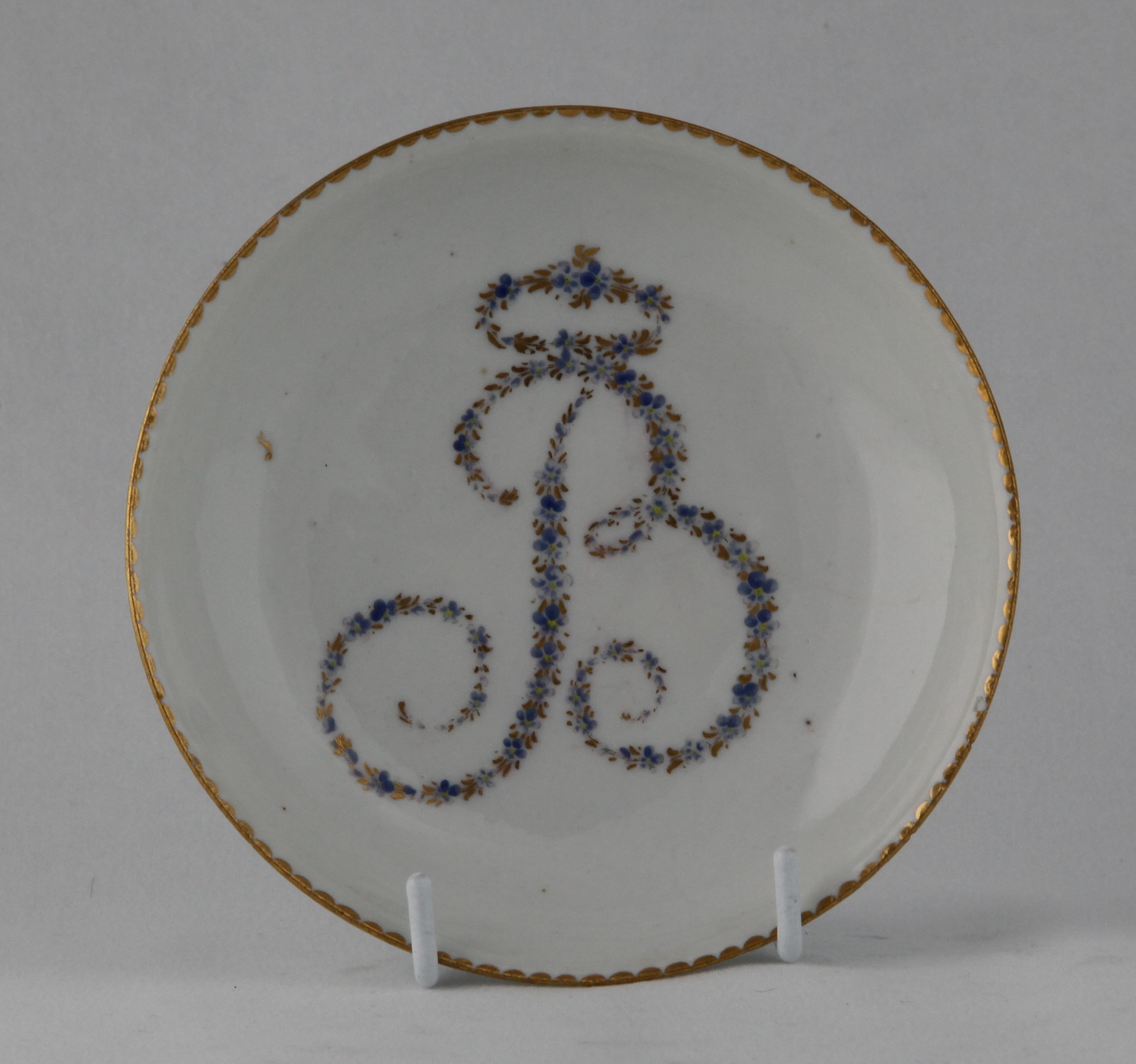 A rare Bristol tea saucer, from the Brice Service, with the large initial 'B' in tiny blue and gilt flowers, within gilt dentil borders, circa 1775, blue painted X marks and the tea bowl with numeral 3 in gilt. Edward Brice was one of Richard Champion's original partners, and this service remained with his family until 1882