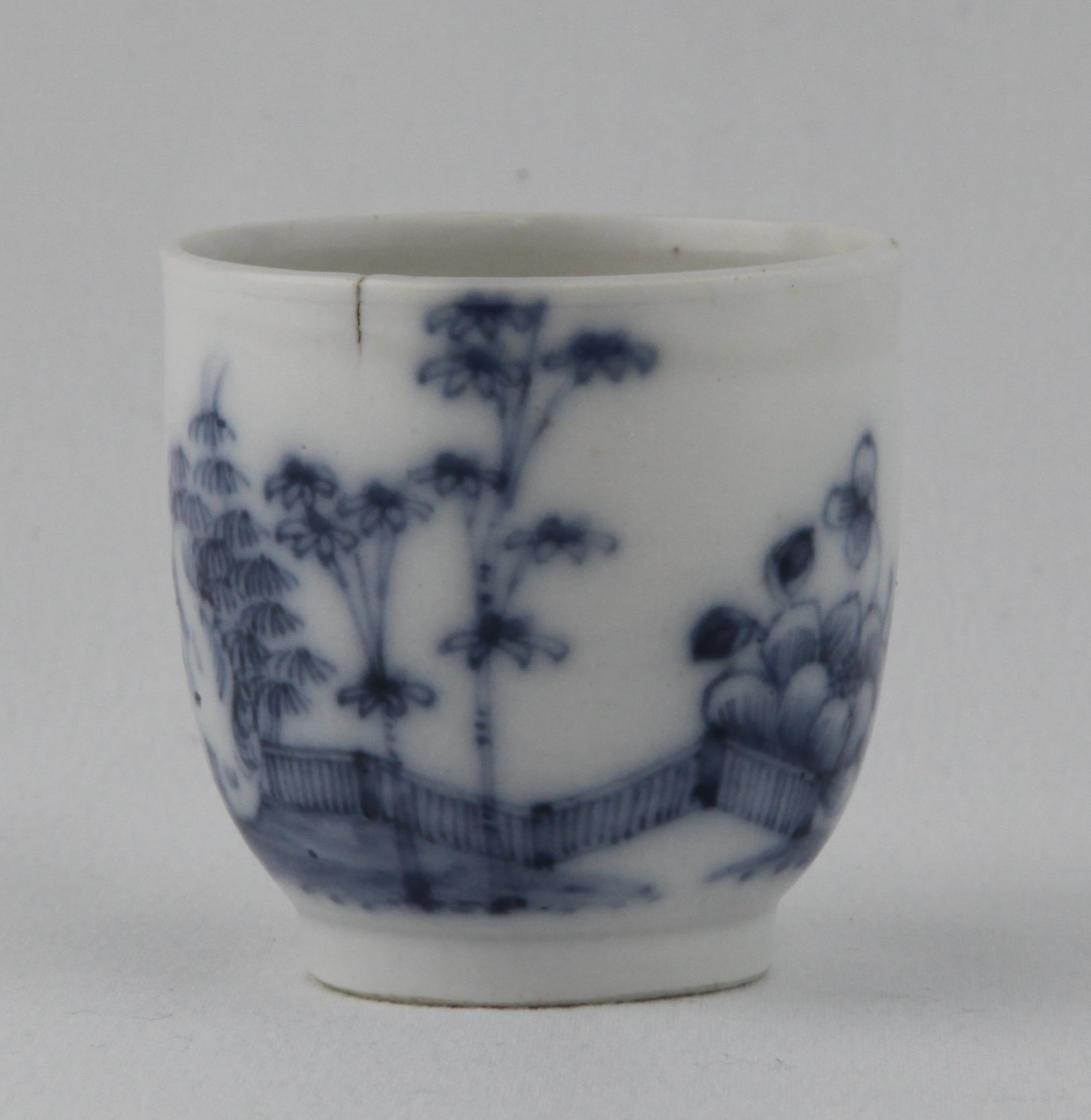 A Plymouth blue/white coffee cup with notched loop handle painted in underglaze blue in Chinese style with bamboo and peony in a fenced garden, 2 1/8” high, circa 1770, traces of blue painted tin mark. Named here as The Bamboo and Dotted Leaf Pattern