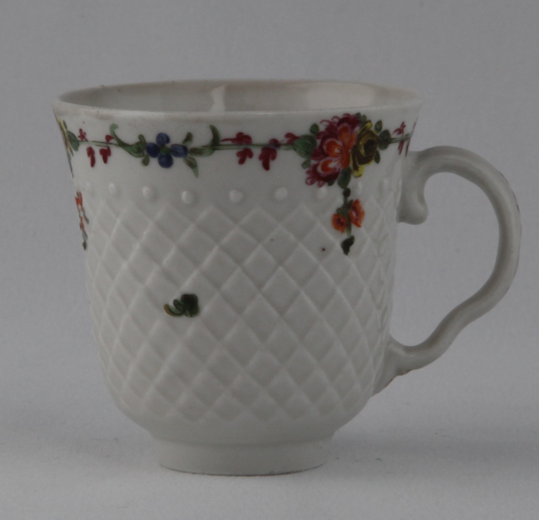 A Bristol coffee cup, with ear shaped handle, painted in coloured enamels with a band of flowers and leaves, above a pinecone moulded ground, 2 5/8" high, circa 1775, no mark