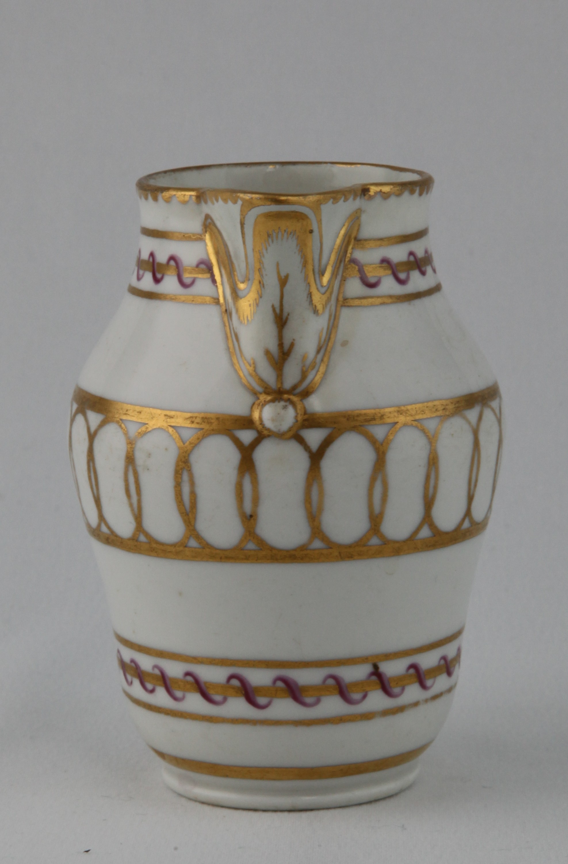A Bristol slender ovoid milk jug, with crabstock loop handle and stiff leaf moulded lip, decorated in puce and gilt with interlinked roundel and scroll bands, gilt dentil rim, 4 1/4" high, circa 1772, blue painted X mark
