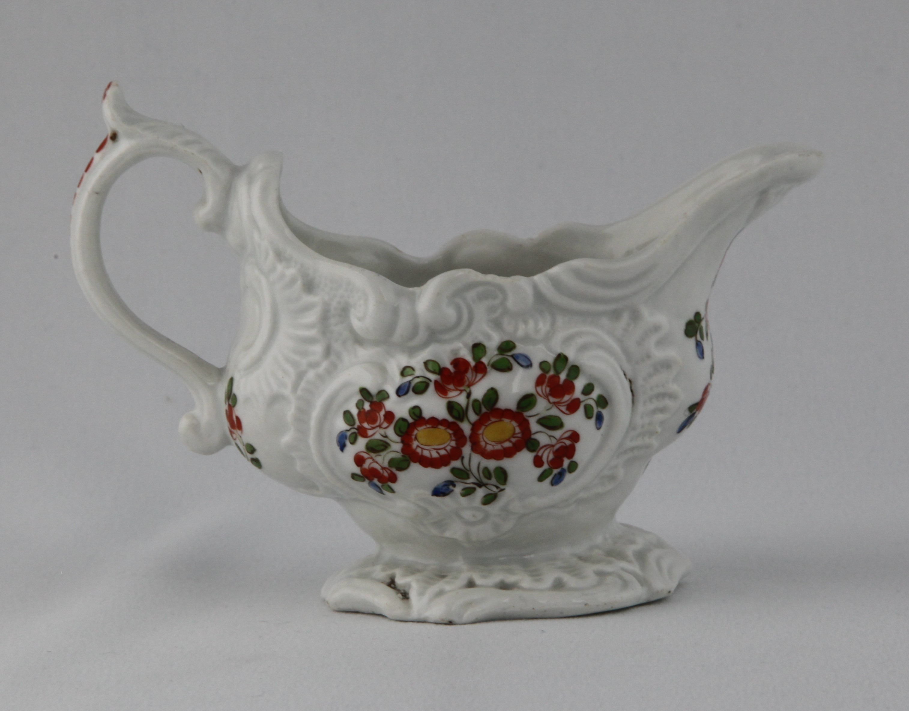 A Plymouth oval sauceboat, with 'C' scroll handle, with scroll thumb piece, painted in Japanese Kakiemon style with flowers and leaves, within 'C' scroll moulded cartouches, beneath a scroll moulded rim, on spreading foot, the interior painted with a flower to the base and the lip, 5 1/4" long, circa 1770, painted tin mark in red