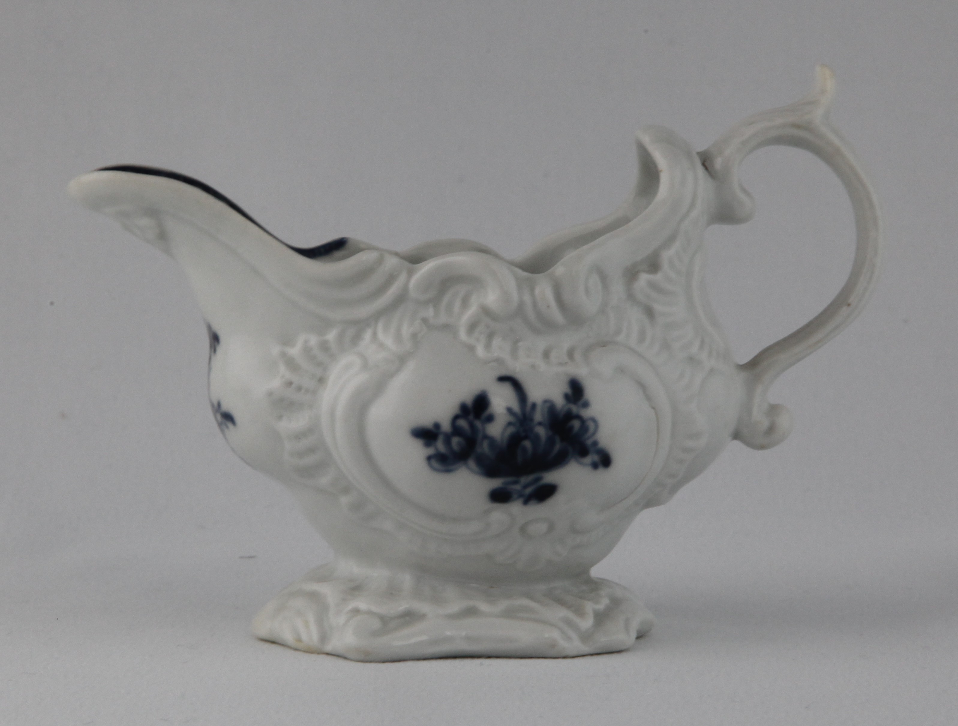 A Plymouth oval sauceboat, of rococo scroll moulded form, with 'C' scroll handle, painted in underglaze blue in Chinese style with flowers and leaves, within  'C' scroll moulded cartouches, the interior of the lip with a cell diaper band, on shell moulded foot, 5 1/2" long, circa 1770, blue painted tin mark