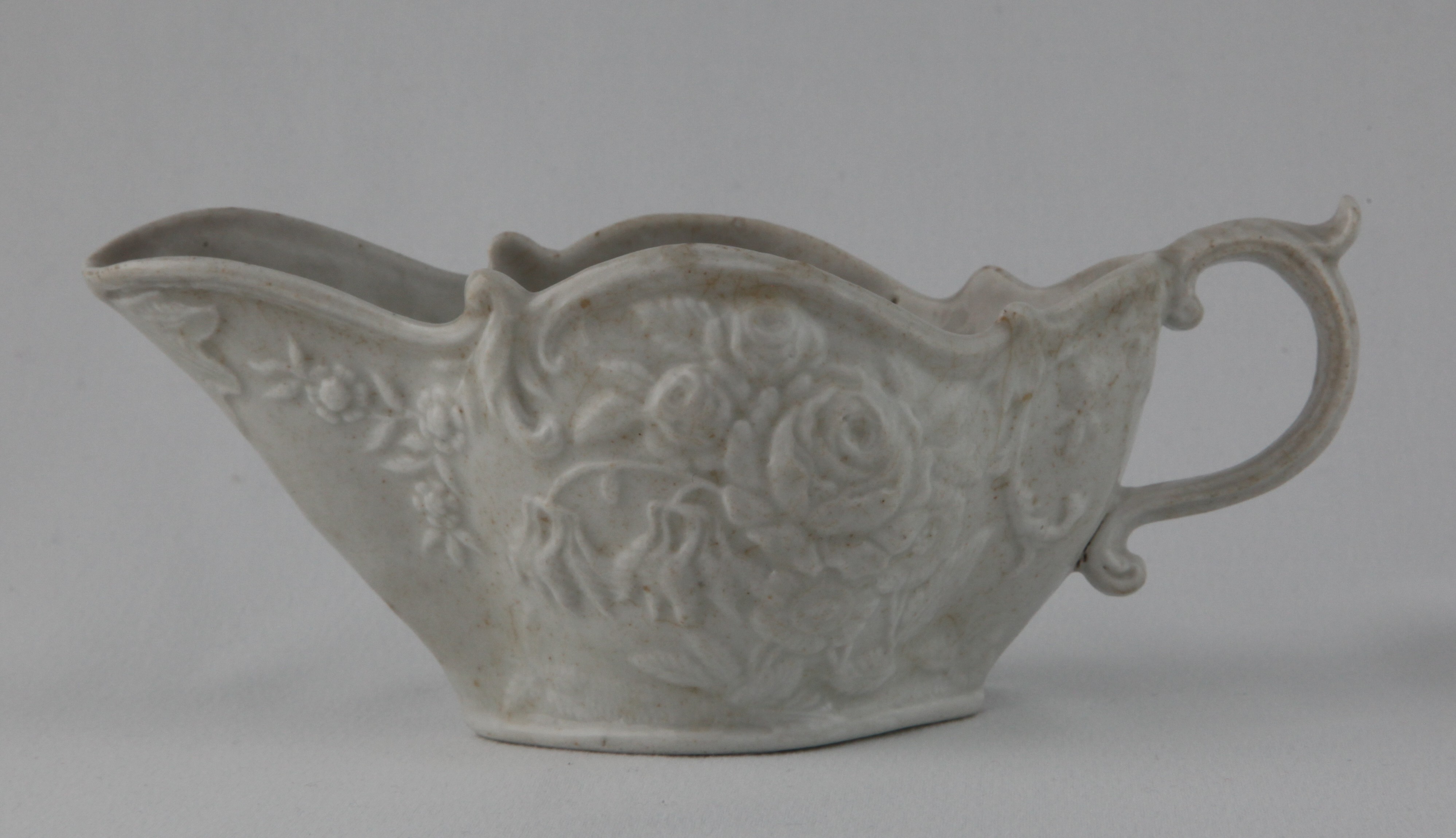 A Bristol oval sauceboat, in the white, the 'S' scroll handle with leaf moulded thumb piece, moulded in bold relief with two sprays of flowers and leaves, and with a leaf beneath the lip, 7 1/4" long, circa 1775, no mark