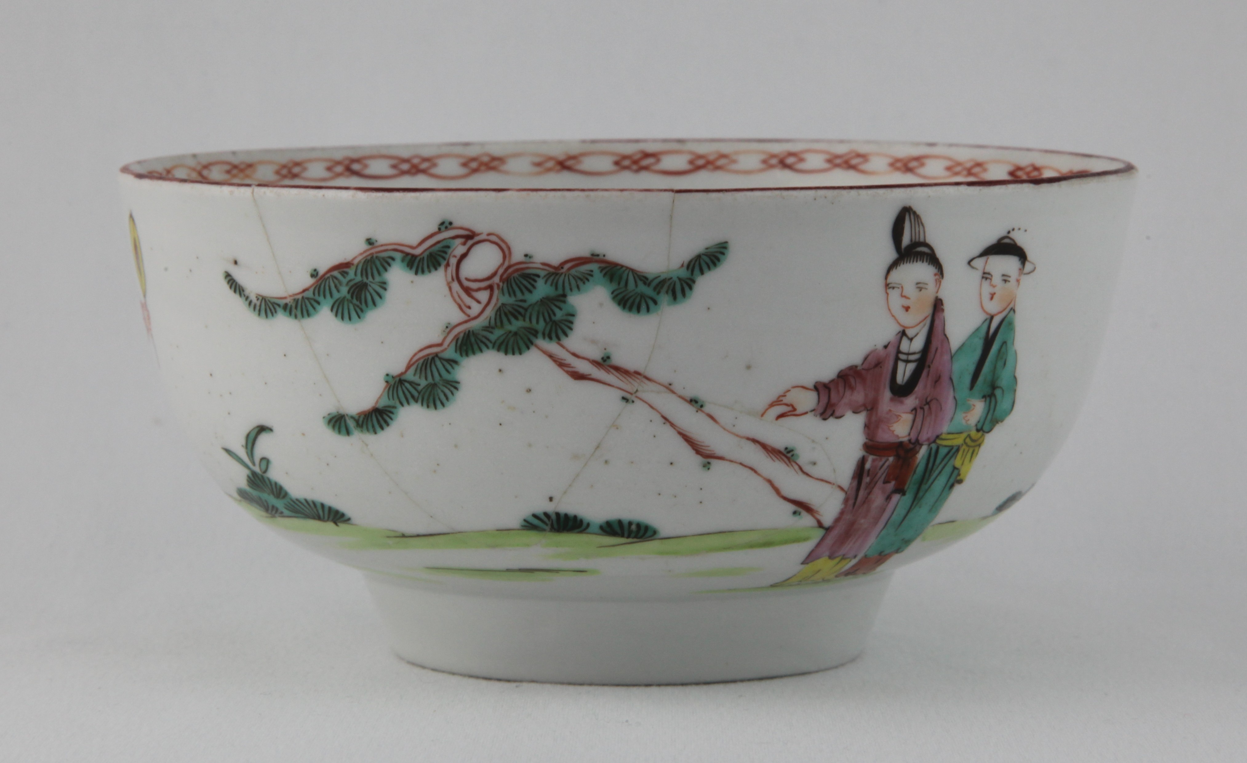 A Bristol round bowl, the exterior painted in Chinese famille rose style with three figures in a garden, in a continuous landscape, beneath a brown line rim, the interior painted with an iron red interlinked band, 5 3/4" diameter, circa 1775, blue painted X and numeral 7 marks