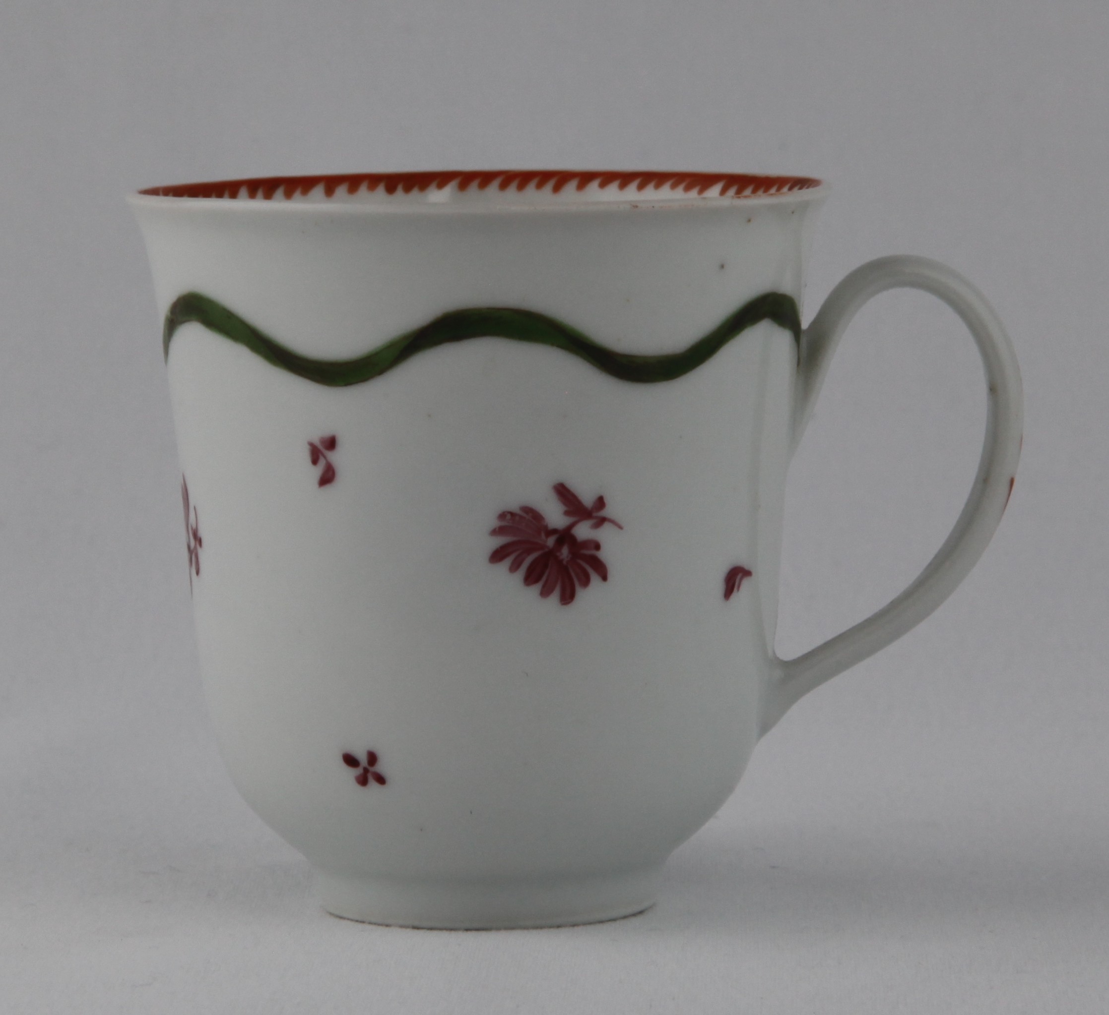 An unusual Bristol tall coffee or chocolate cup, with flared rim and loop handle, painted in puce monochrome with flower sprigs, beneath a wavy green band, the interior with an angular orange dentil band, 2 3/4" high, circa 1775, no mark