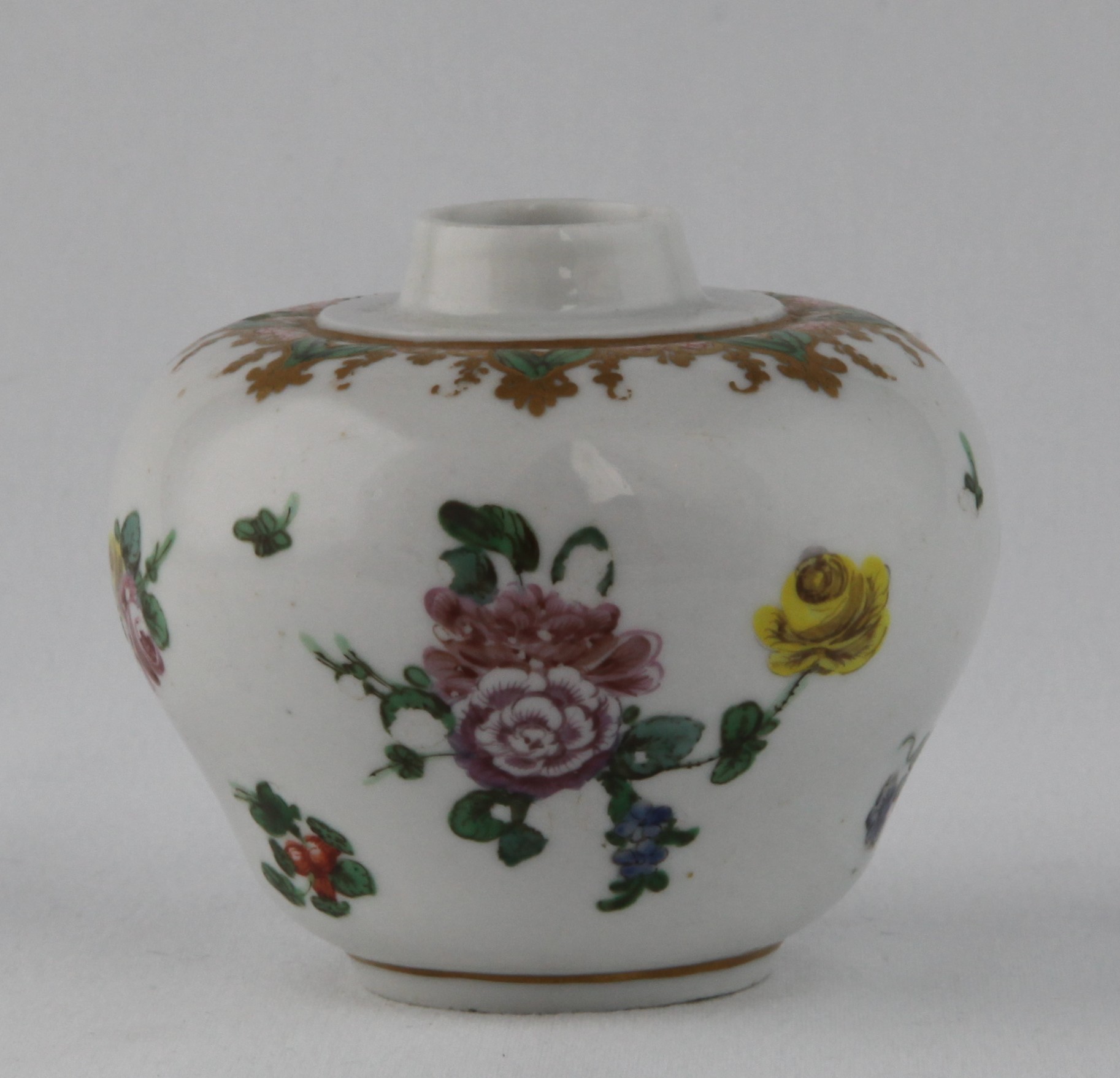 A rare Bristol small ogee shaped tea canister, with short straight neck, painted in coloured enamels with two sprays of flowers and leaves, and scattered flowers, beneath a gilt leaf scroll band, with iron red scroll panale and green leaves, 2 1/2" high, circa 1772, no mark