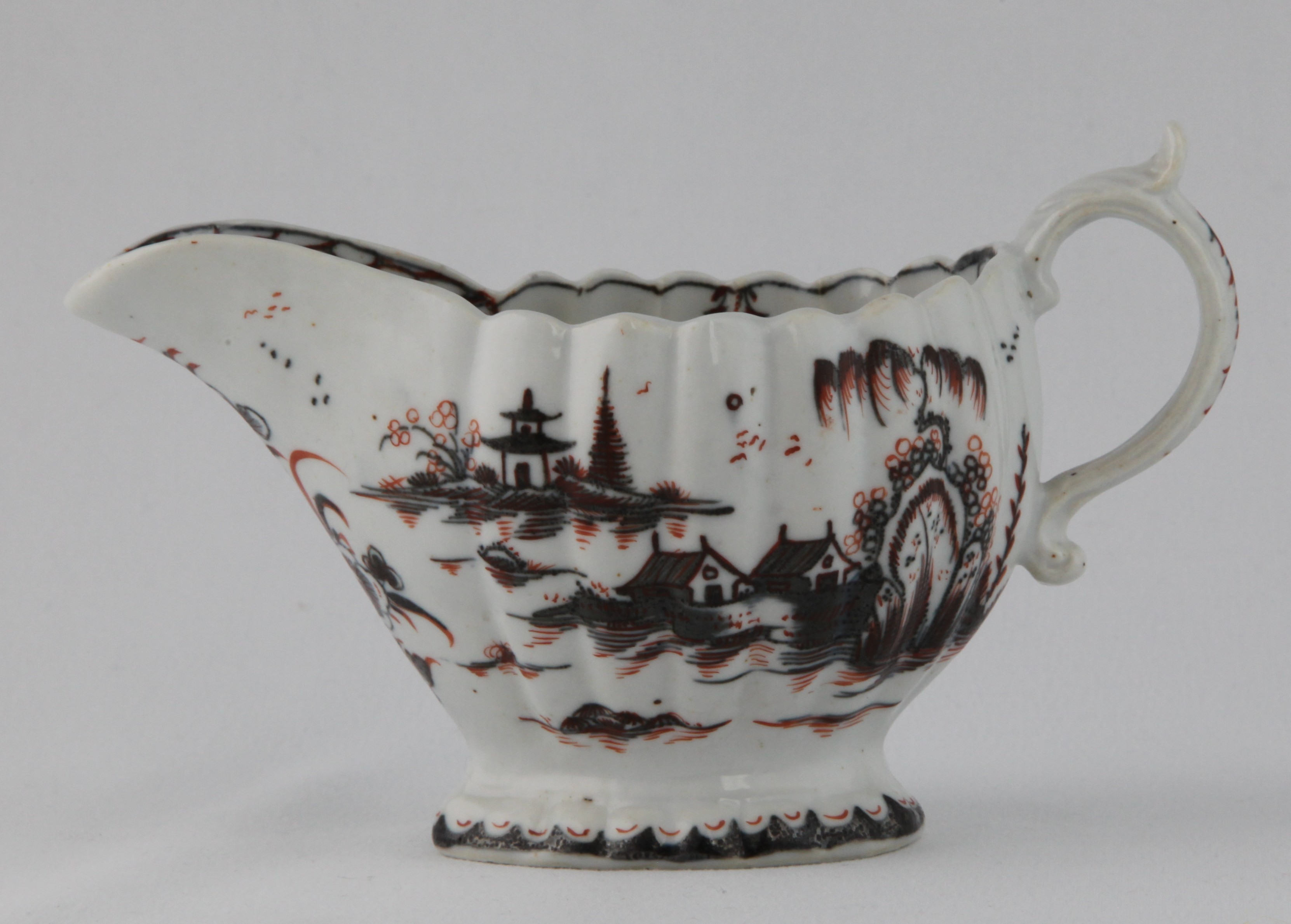 A Plymouth fluted oval sauceboat, the 'S' scroll handle with leaf moulded thumb piece, painted in underglaze blue in Chinese style with buildings, pine trees and rockwork, in a river landscape, picked out in iron red, the interior painted with a flower, within a pendant flower and line border, the lip painted with a flower, within a cell diaper cartouche, 6 1/4" long, circa 1770