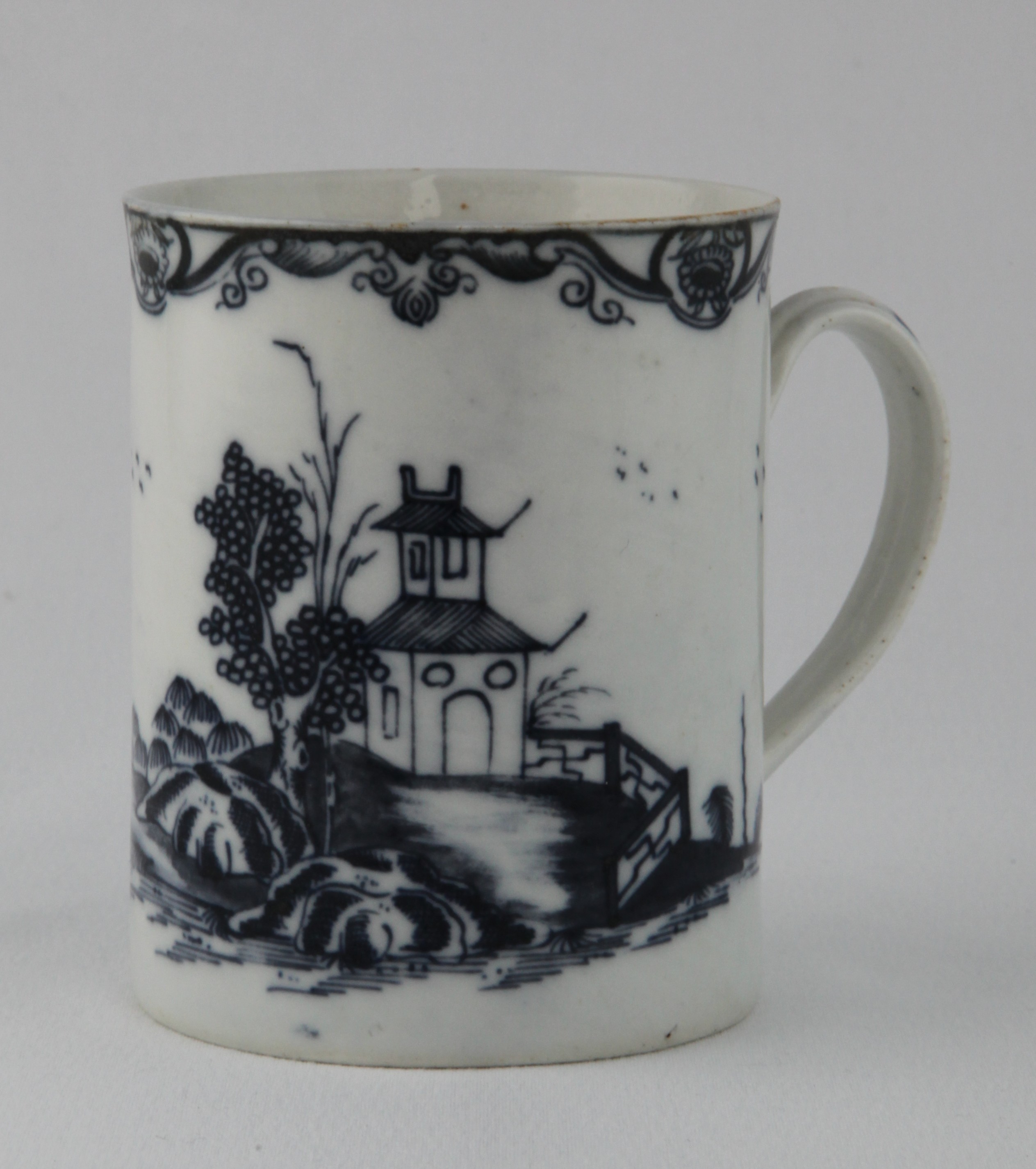 A Plymouth cylindrical mug, with notched loop handle, painted in underglaze blue with a pagoda, in a fenced garden, in a Chinese river landscape, beneath a flower and scroll border, 3 3/4" high, circa 1770