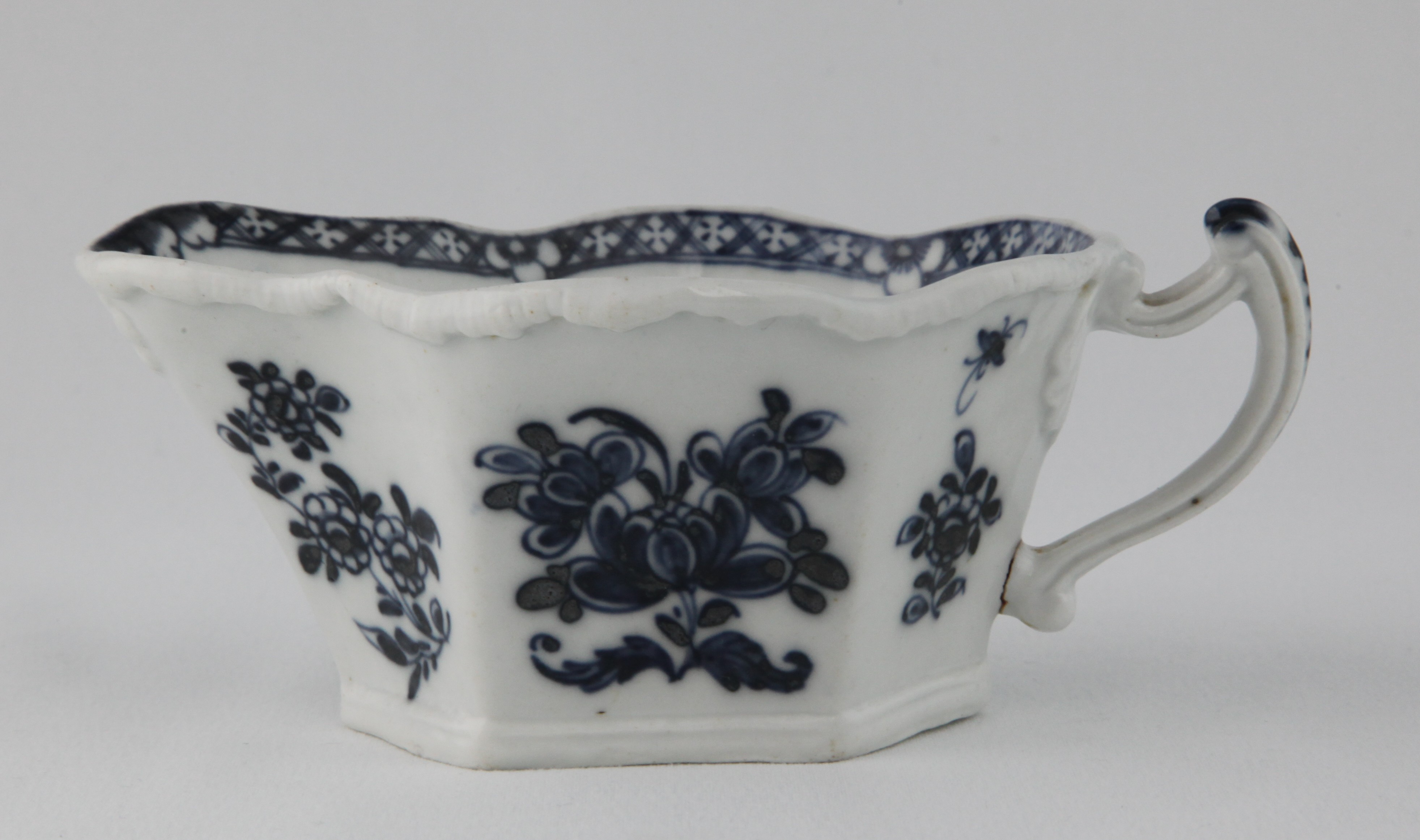 A Plymouth hexagonal sauceboat, with angular loop handle, the exterior painted in underglaze blue in Chinese style with sprays of flowers and leaves, beneath a flower head and 'melting ice' moulded border, the interior painted with a flower head, within a flower and diaper border, 5 3/4" long, circa 1770, blue painted tin mark