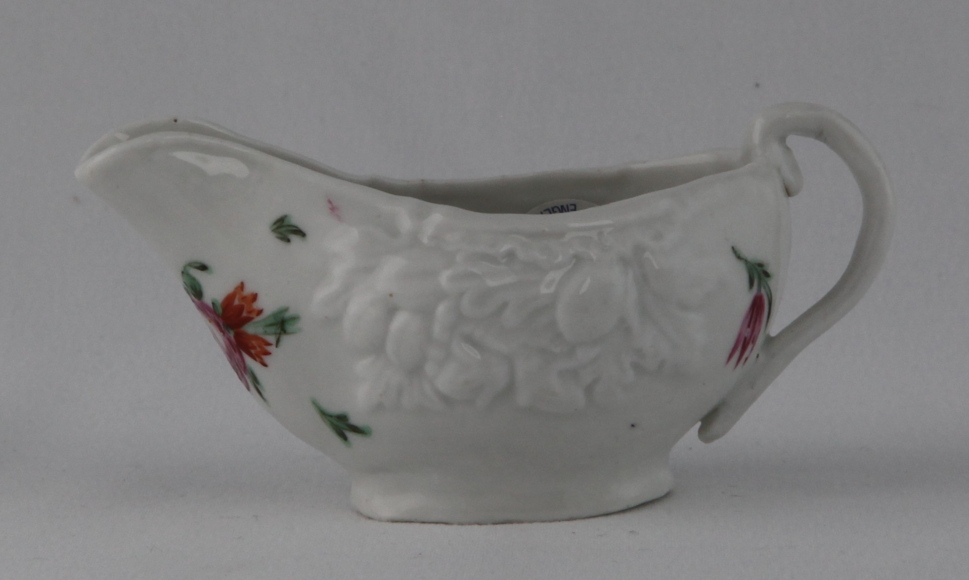 A Bristol small oval butter boat, with loop handle, crisply moulded in relief with two clusters of fruits and leaves, and painted in coloured enamels with a flower spray and scattered flowers and leaves. 4 1/4" long, circa 1770, blue X14