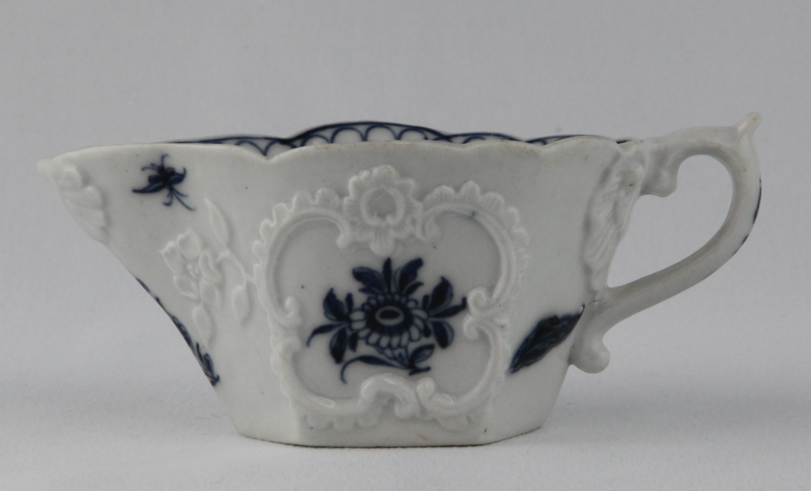 A Plymouth small hexagonal sauceboat, the 'S' scroll handle with scroll thumb piece and shell moulded upper terminal, painted in underglaze blue with flowers and leaves, within crisply moulded 'C' scroll cartouches, with trailing flowers and leaves, and painted with two winged insects, the interior with flowers, beneath a looped border, 4 3/4" long, circa 1770, blue painted tin mark